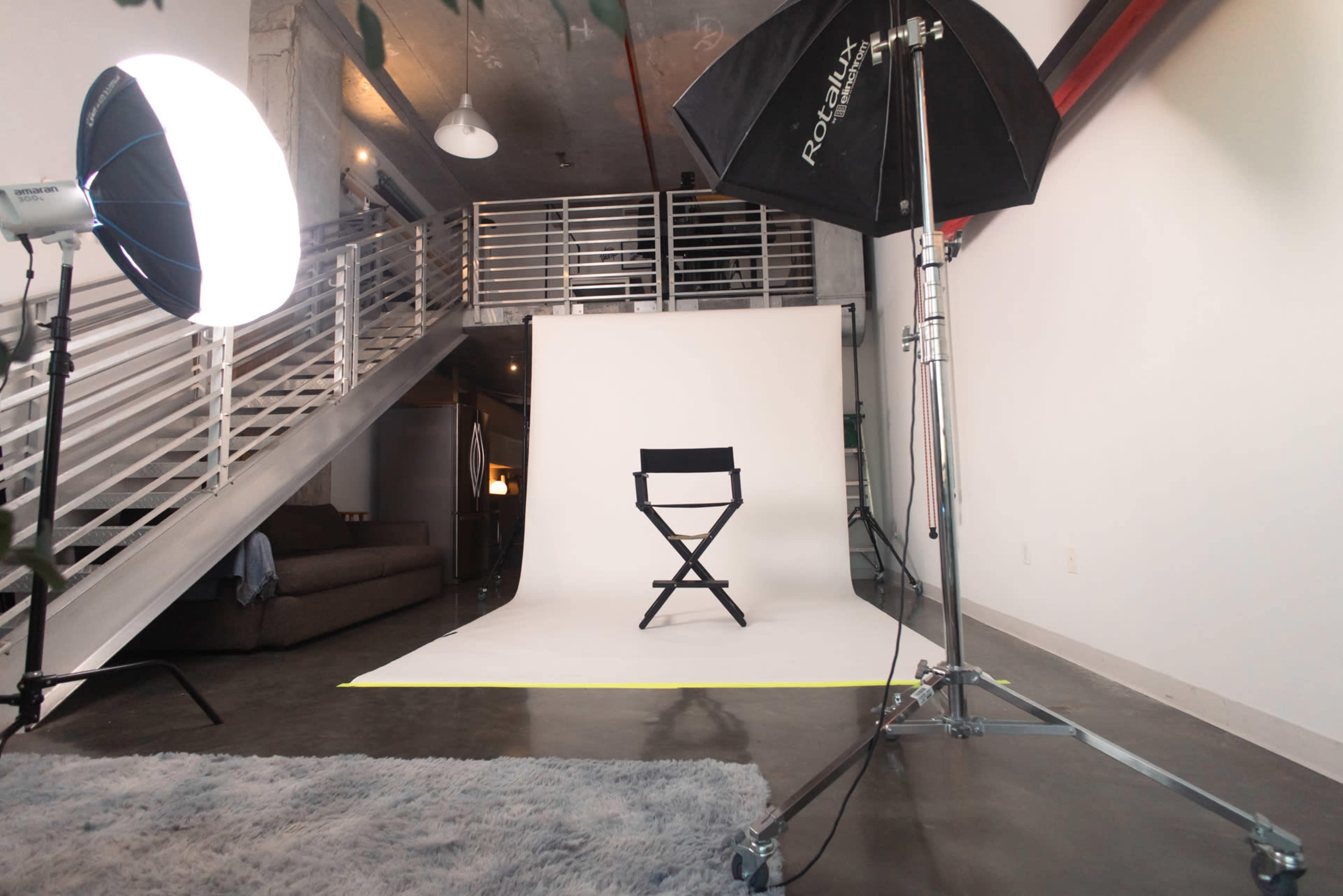 A photography studio setup features a director's chair in front of a backdrop, with softbox lights illuminating the scene.