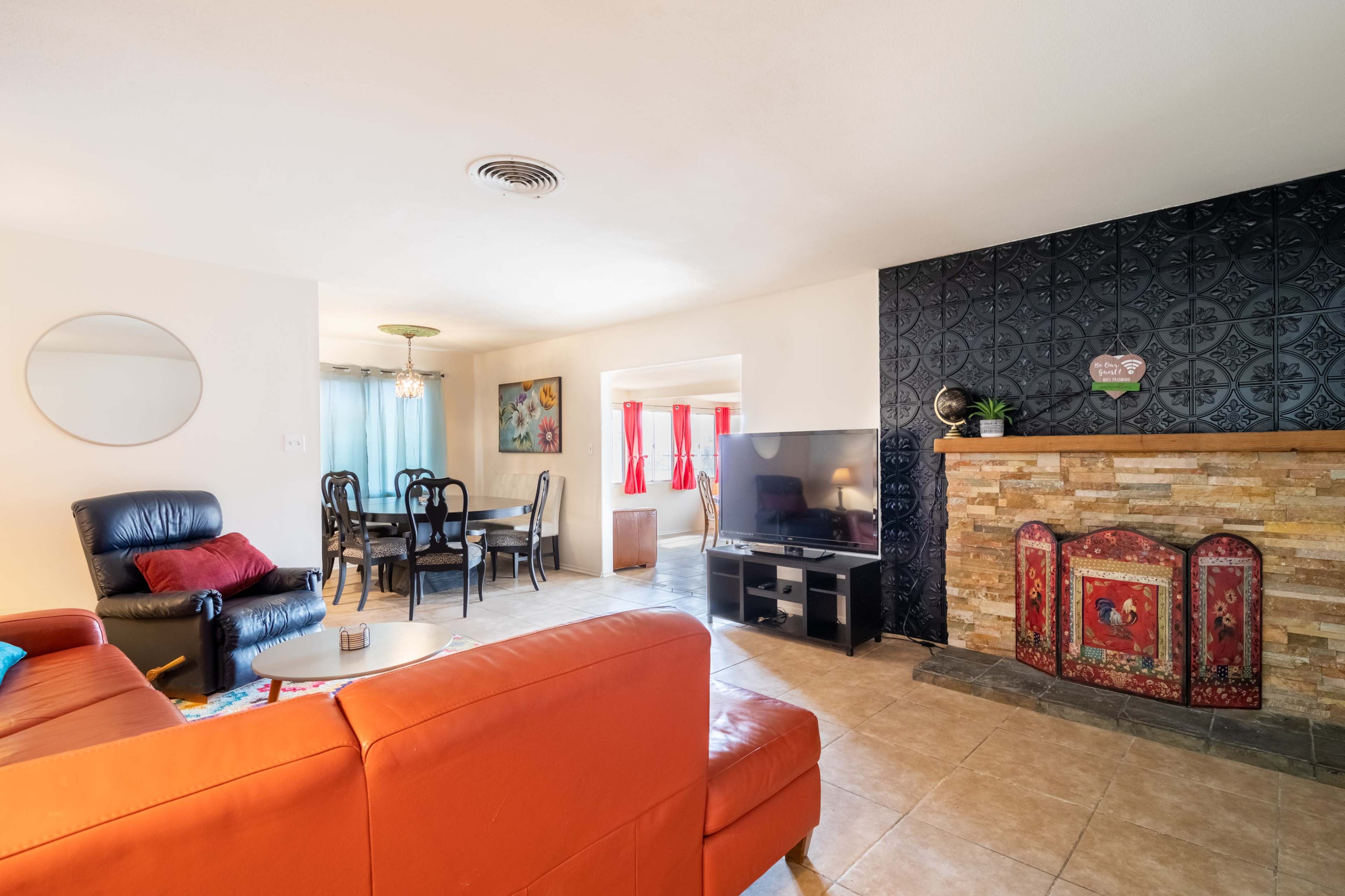 The image shows a living room with a red leather sofa, a television, a stone fireplace, and a dining area in the background.