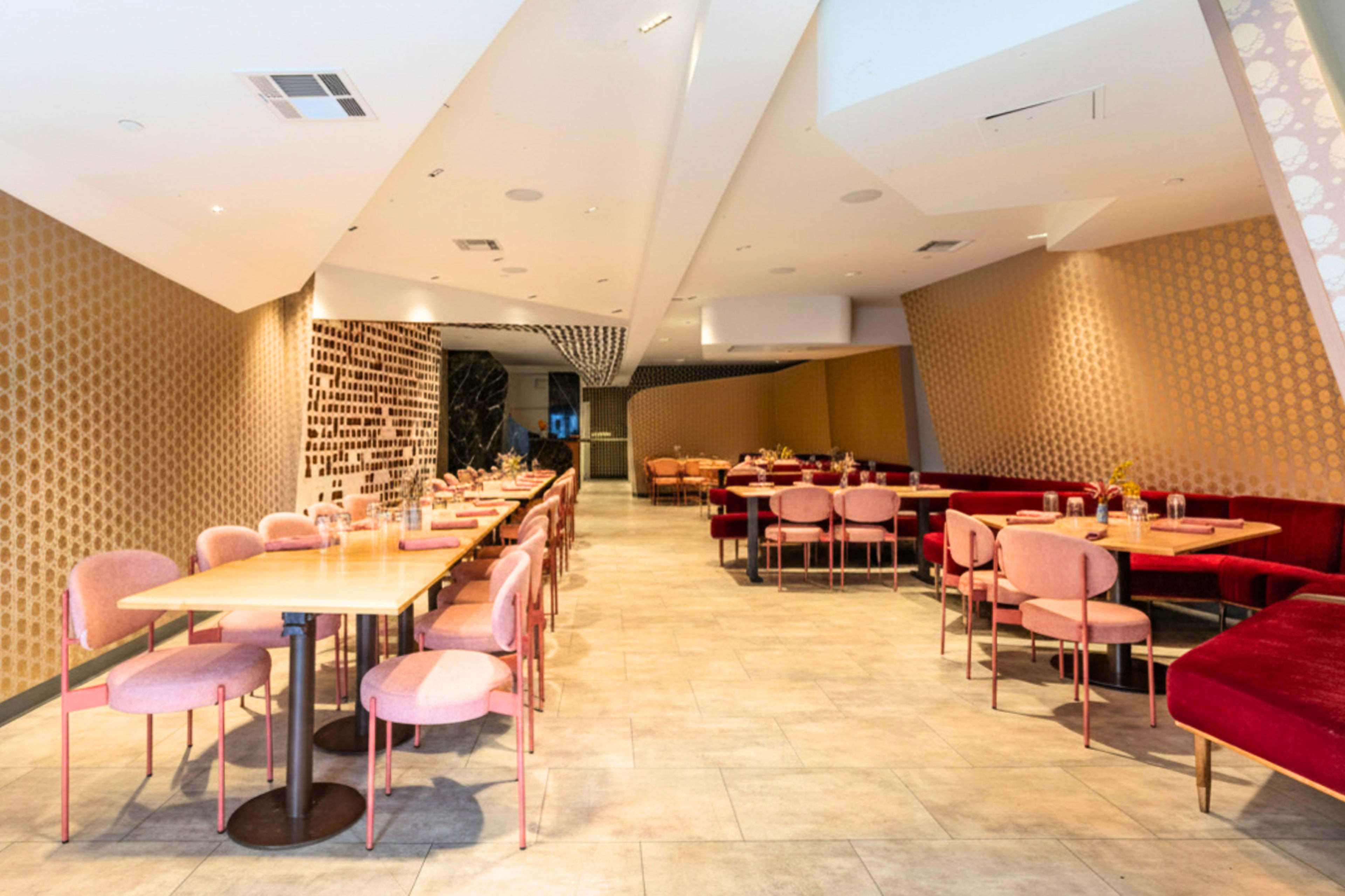 The image shows a modern restaurant interior with pink chairs and wooden tables, featuring patterned walls and open seating areas.