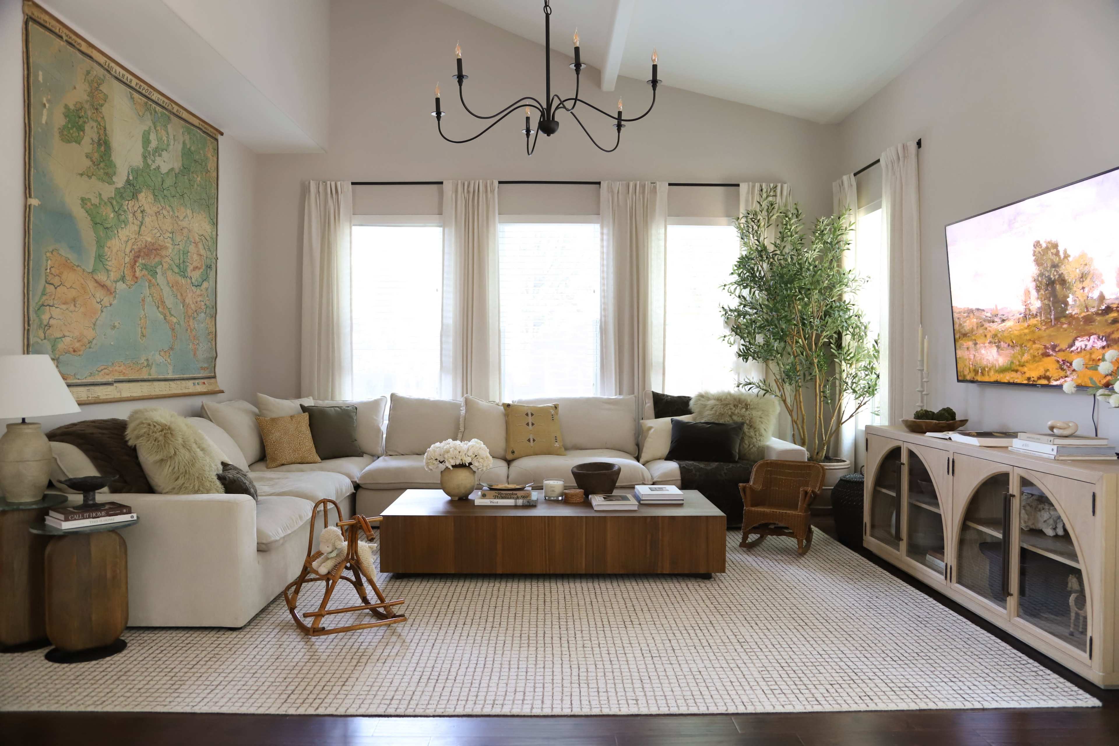 The image shows a well-furnished living room with a large sectional sofa, a wooden coffee table, a wall-mounted television, and a decorative map on the wall.