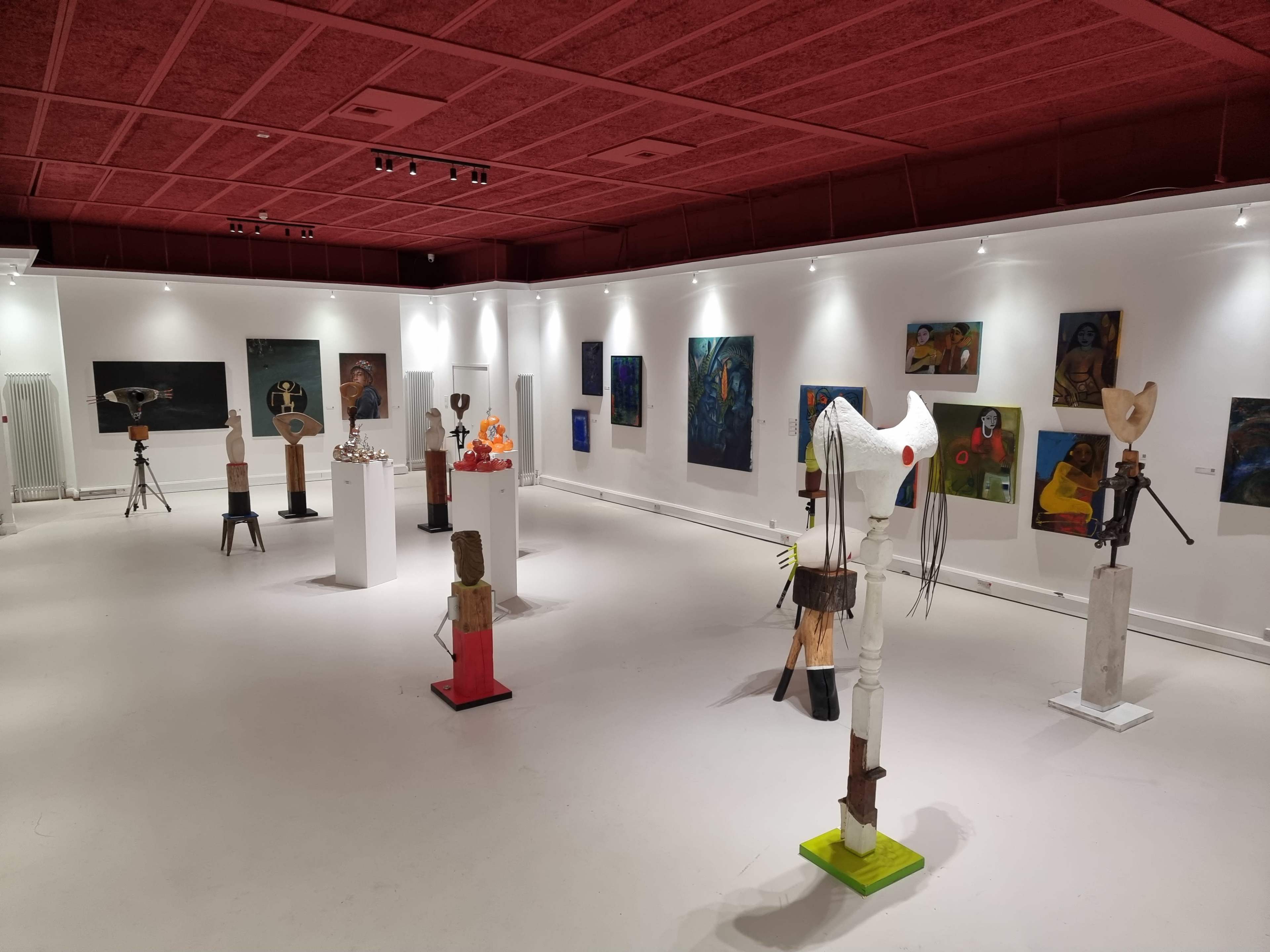 An art gallery featuring various sculptures and paintings displayed on white walls and pedestals.