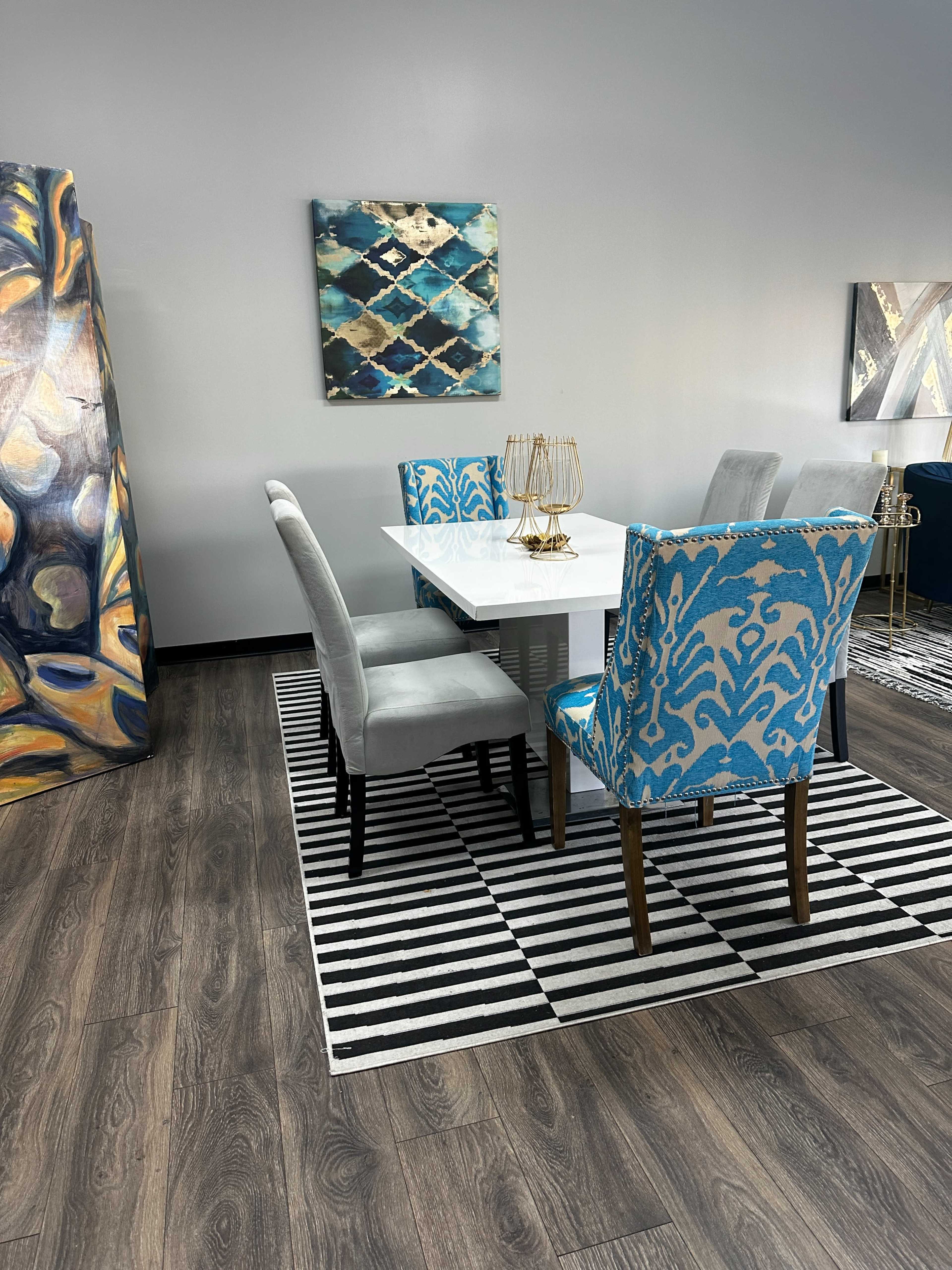 A dining area features a white table surrounded by colorful chairs on a striped rug, with abstract artwork on the walls.