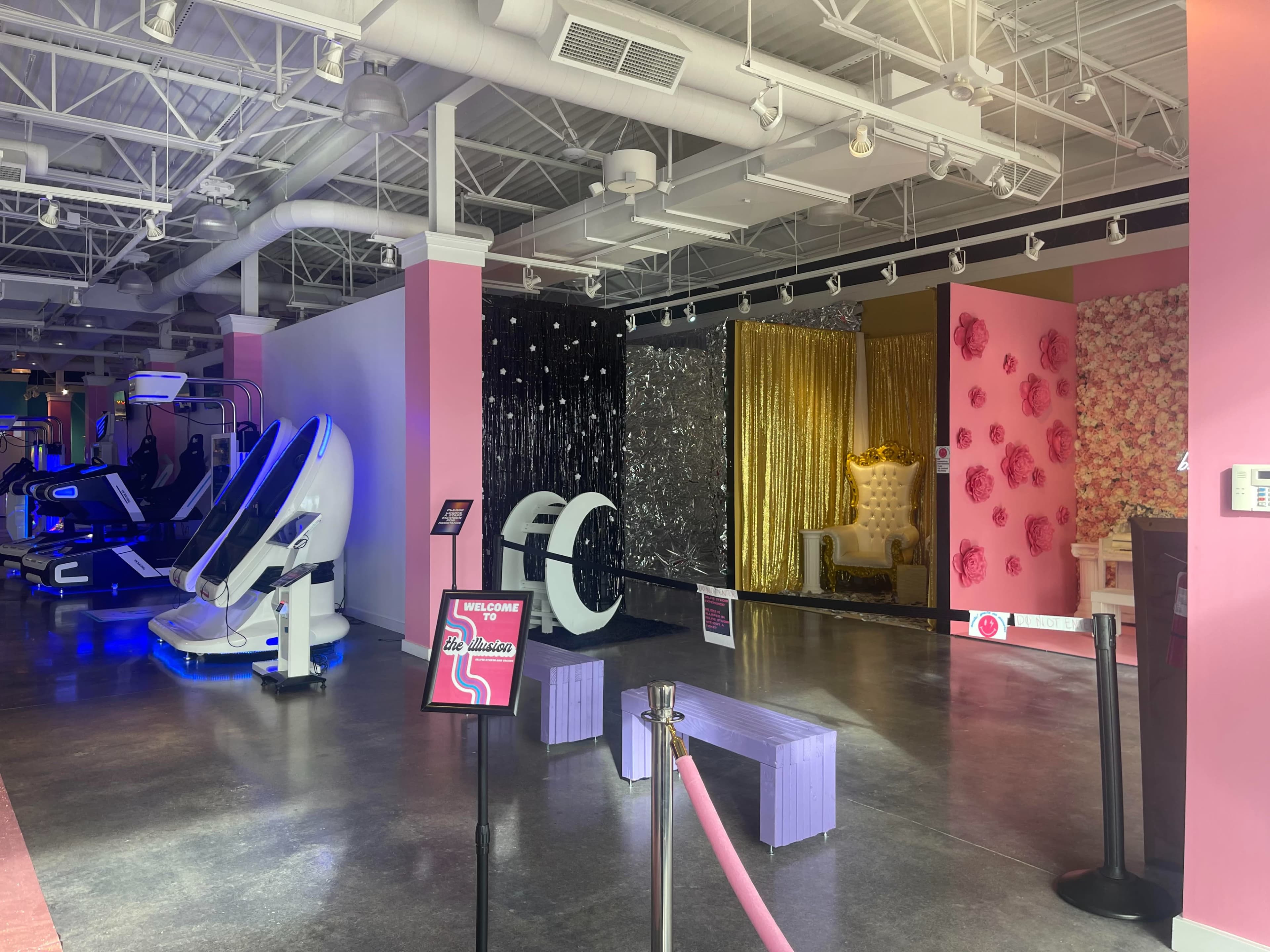 A brightly lit fitness studio with exercise machines on the left and themed decor walls, including a sequined black wall and a golden backdrop, on the right.