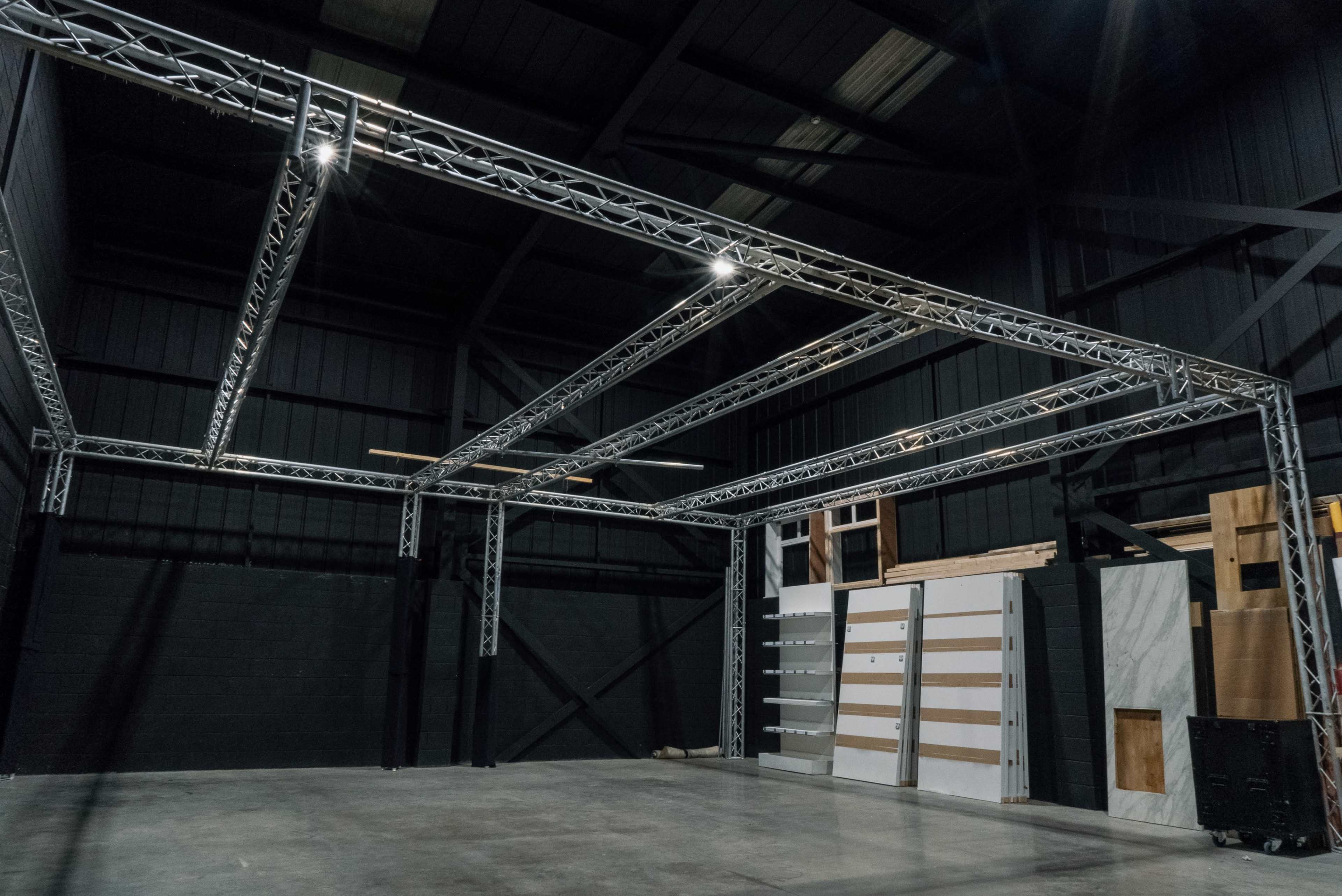 A spacious industrial interior with a metallic truss structure overhead and various panels against the walls.
