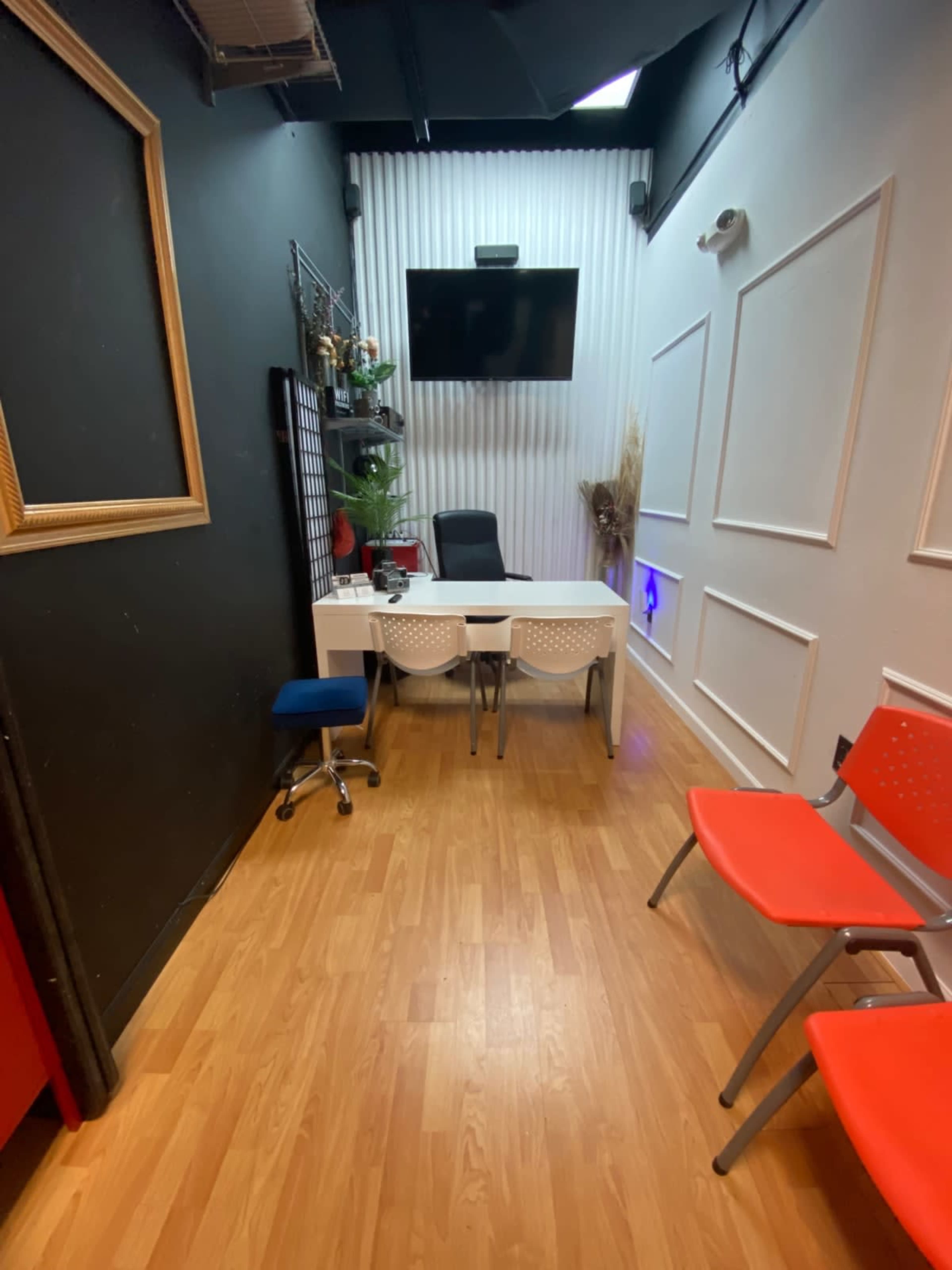 A small office space with a desk and chairs, wooden flooring, and a wall-mounted TV.