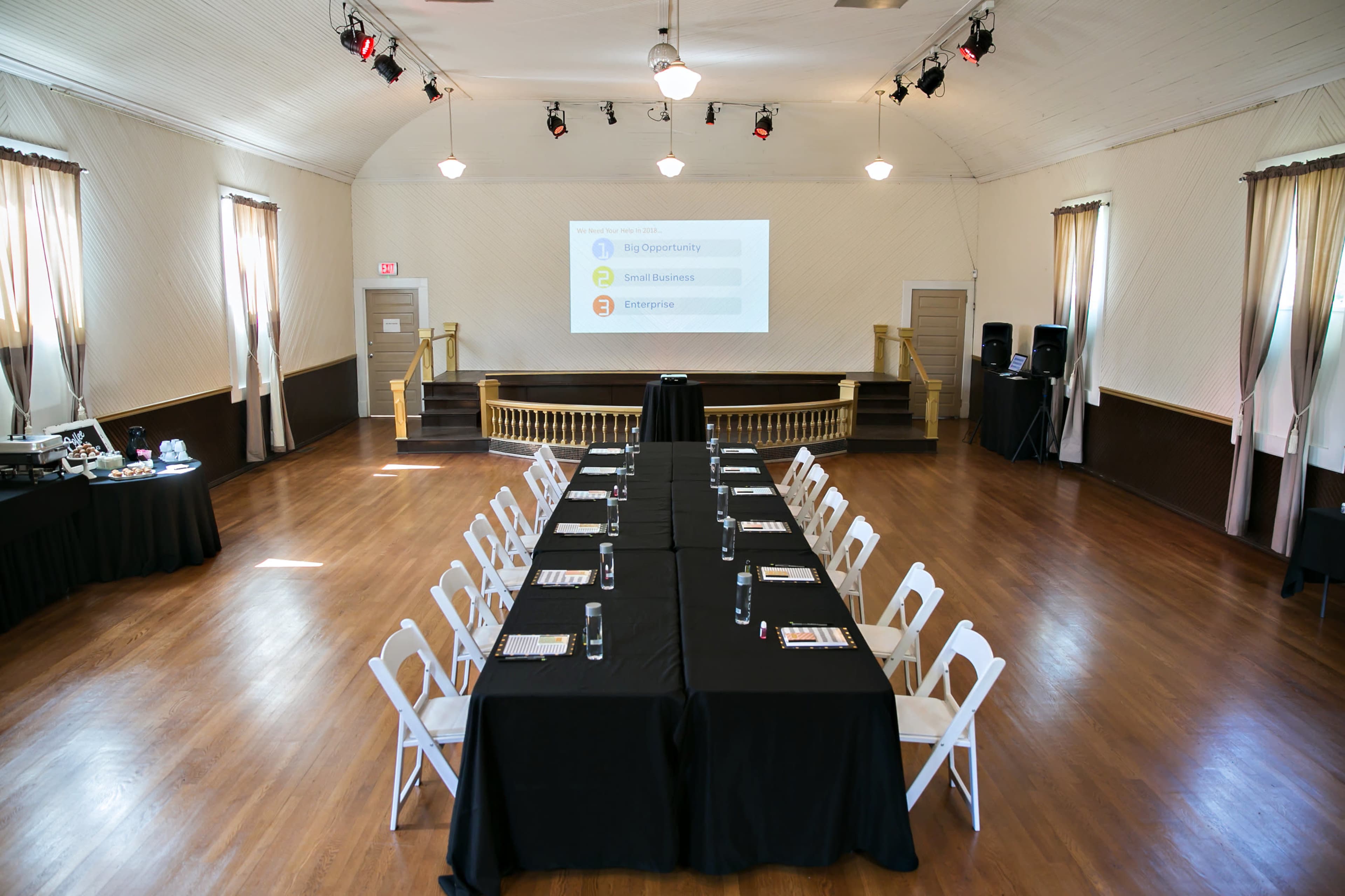 A spacious conference room is set up with a long table covered in black cloth, surrounded by white chairs, and a presentation screen displays three categories at the front.