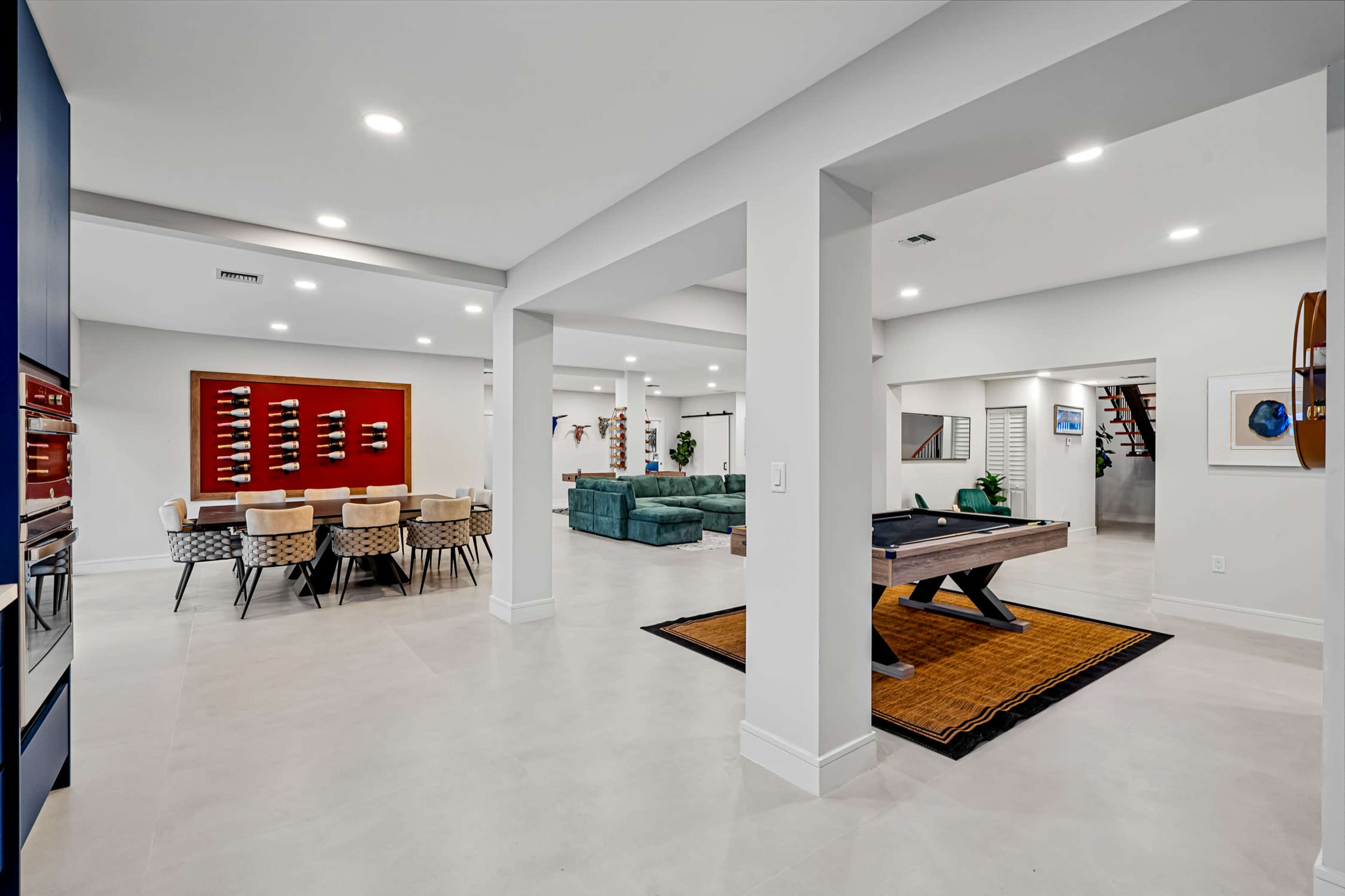 The image shows a modern, open-concept living space featuring a dining area with a table, a living area with a sofa, and a game area with a pool table.