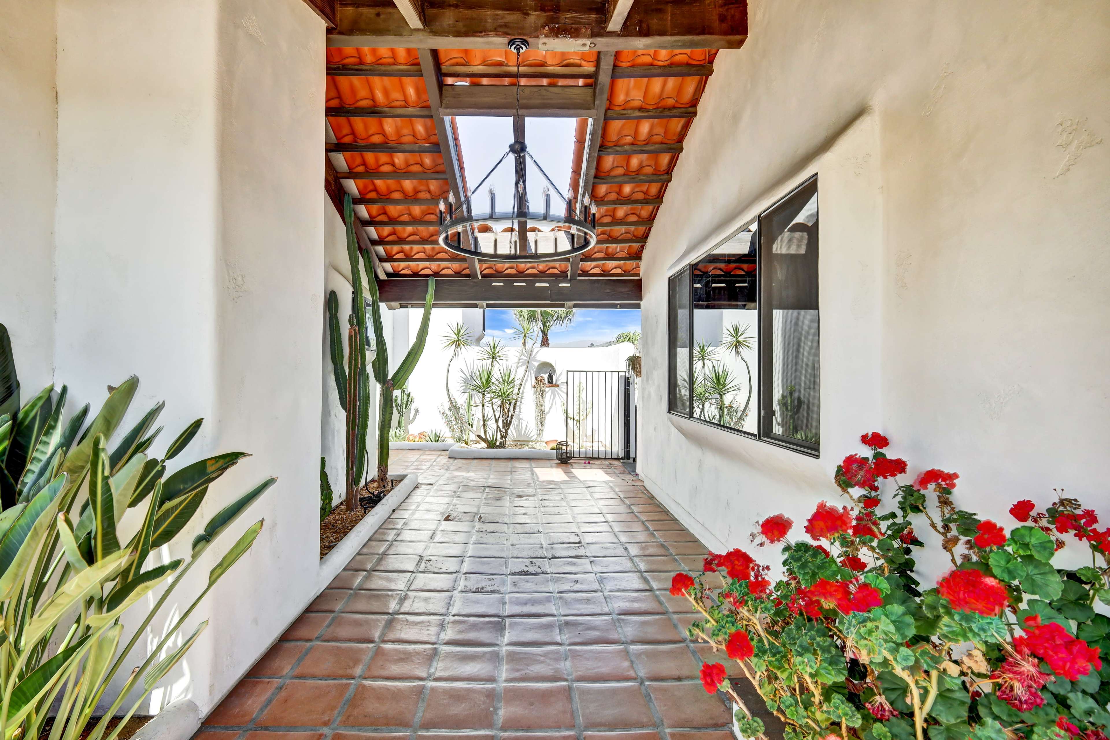 A tiled corridor with potted plants and a decorative chandelier leads to a gated entrance.