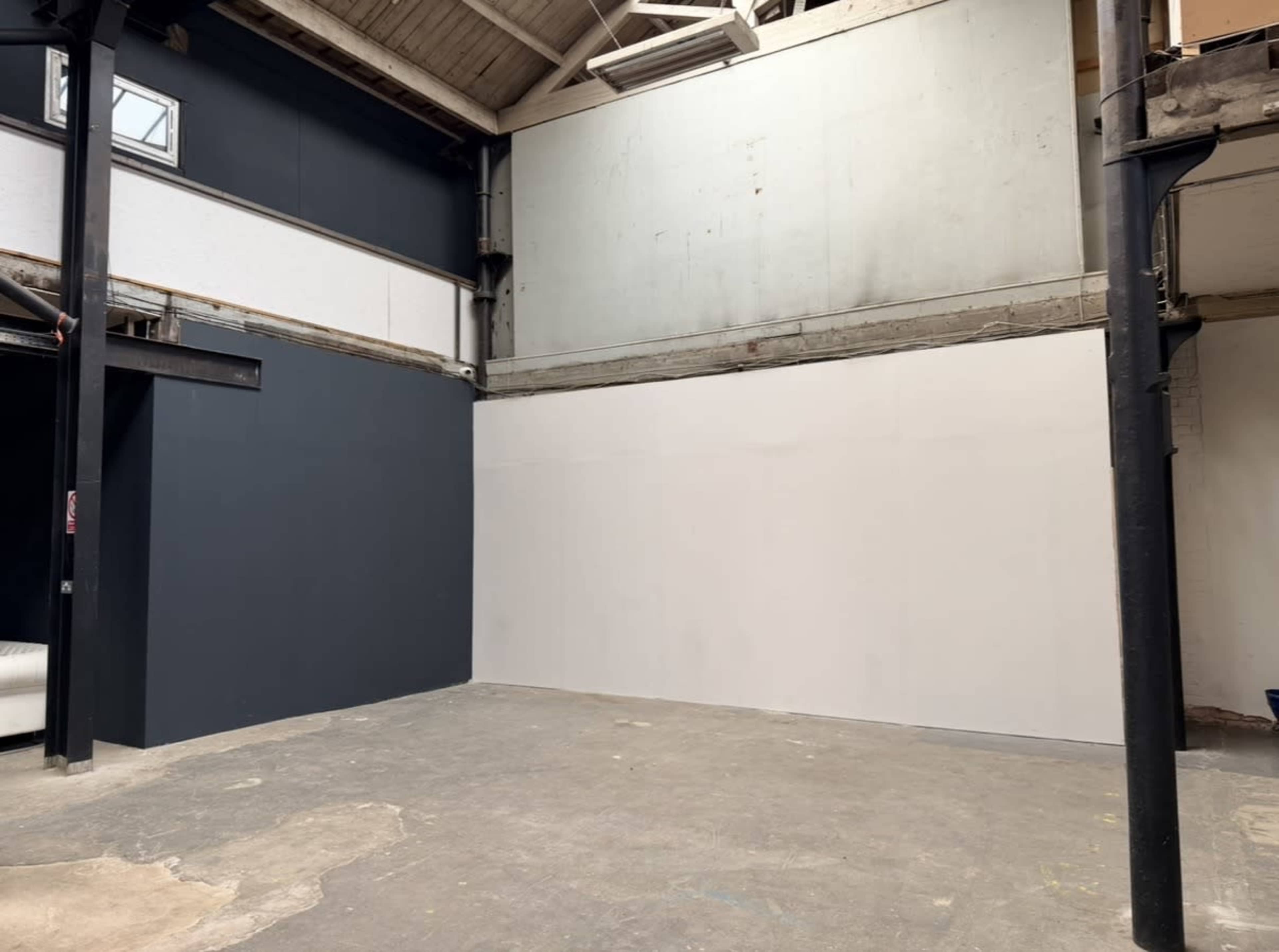 The image shows an empty industrial space with a dark blue wall on one side and a large white wall on the opposite side.