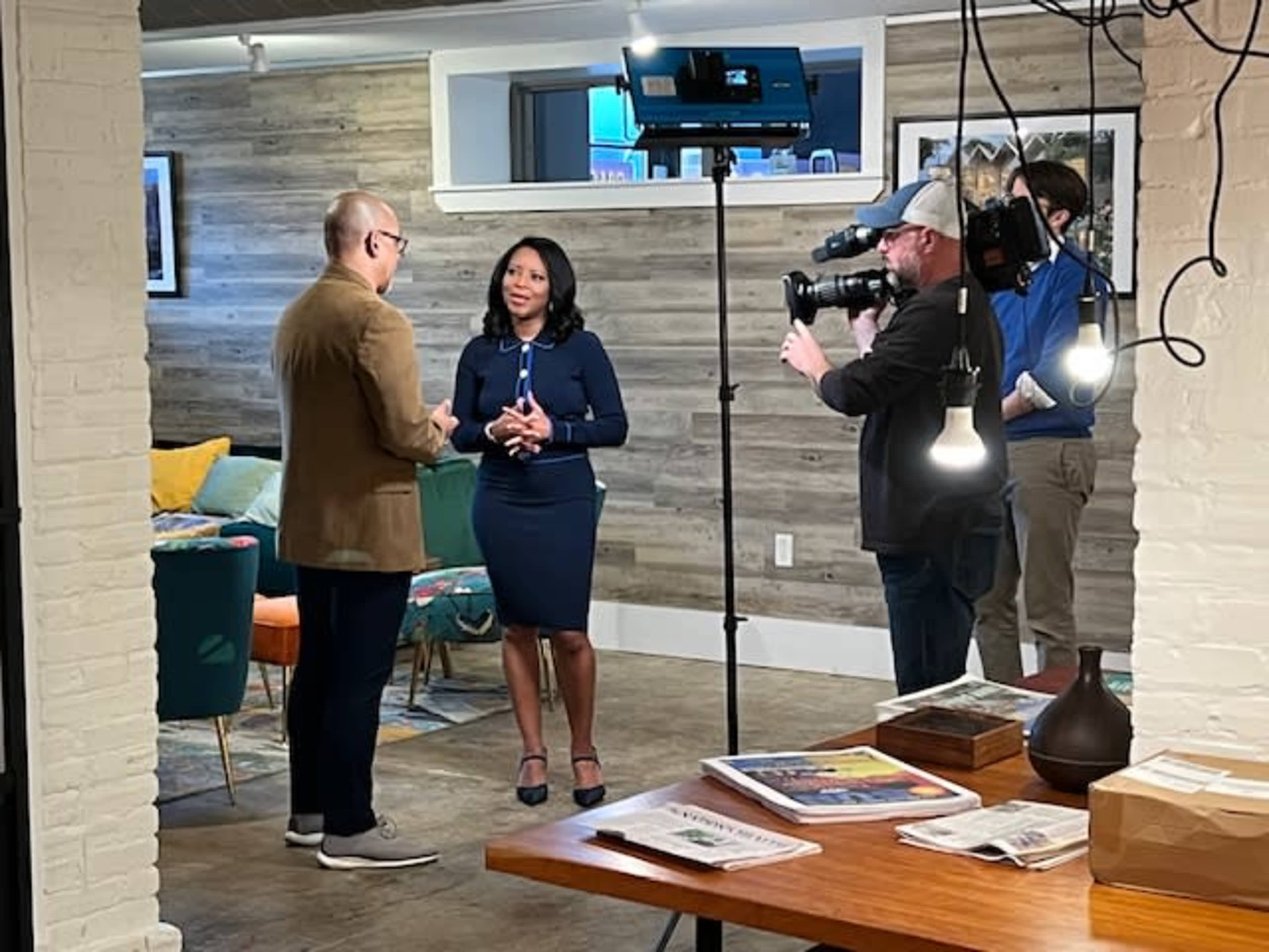 Two people are engaged in a conversation in a well-lit, modern room while a camera crew records the interaction.