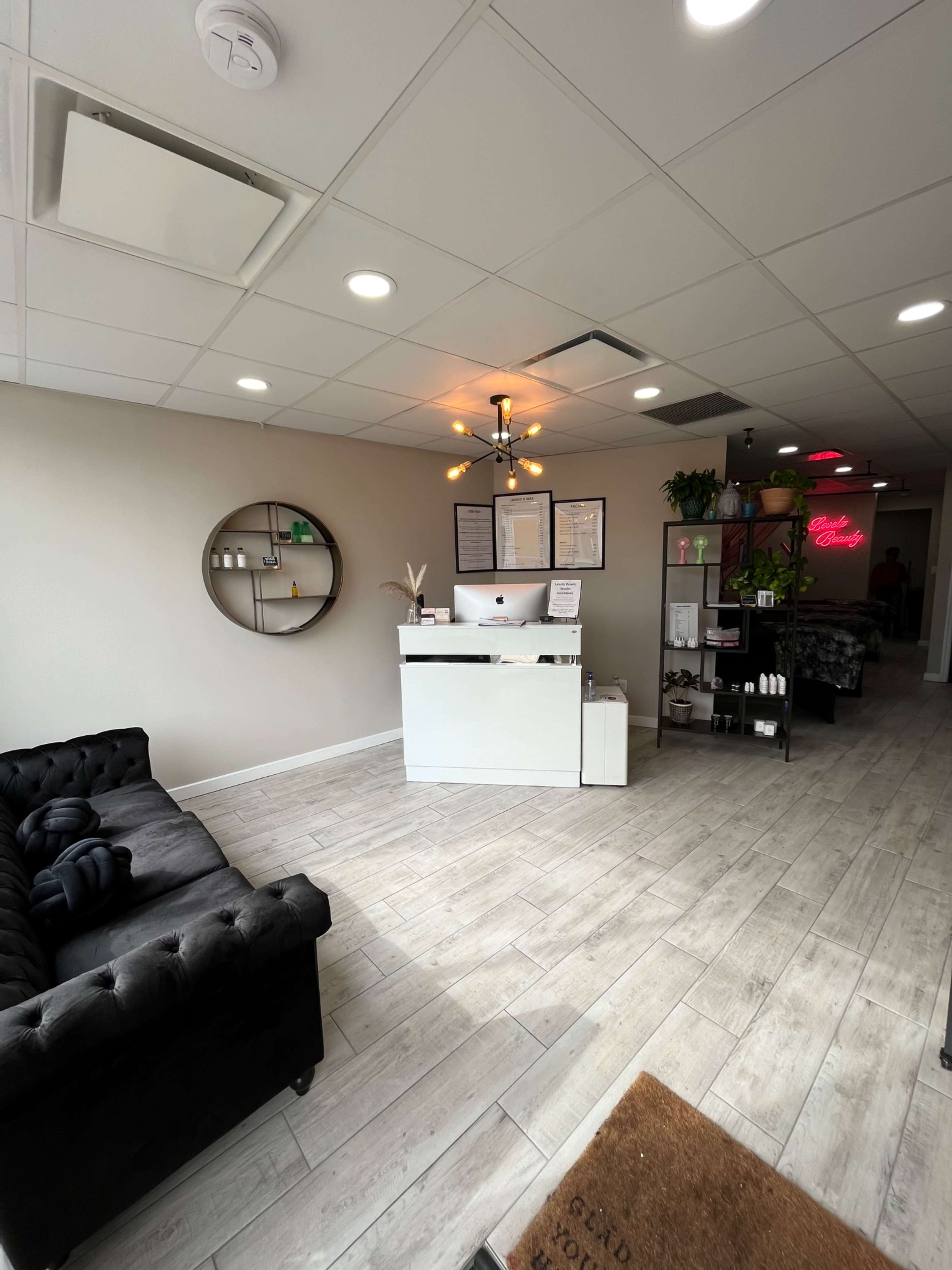 A modern reception area with a white front desk, a black tufted sofa, and various decorative items arranged on the walls and shelves.