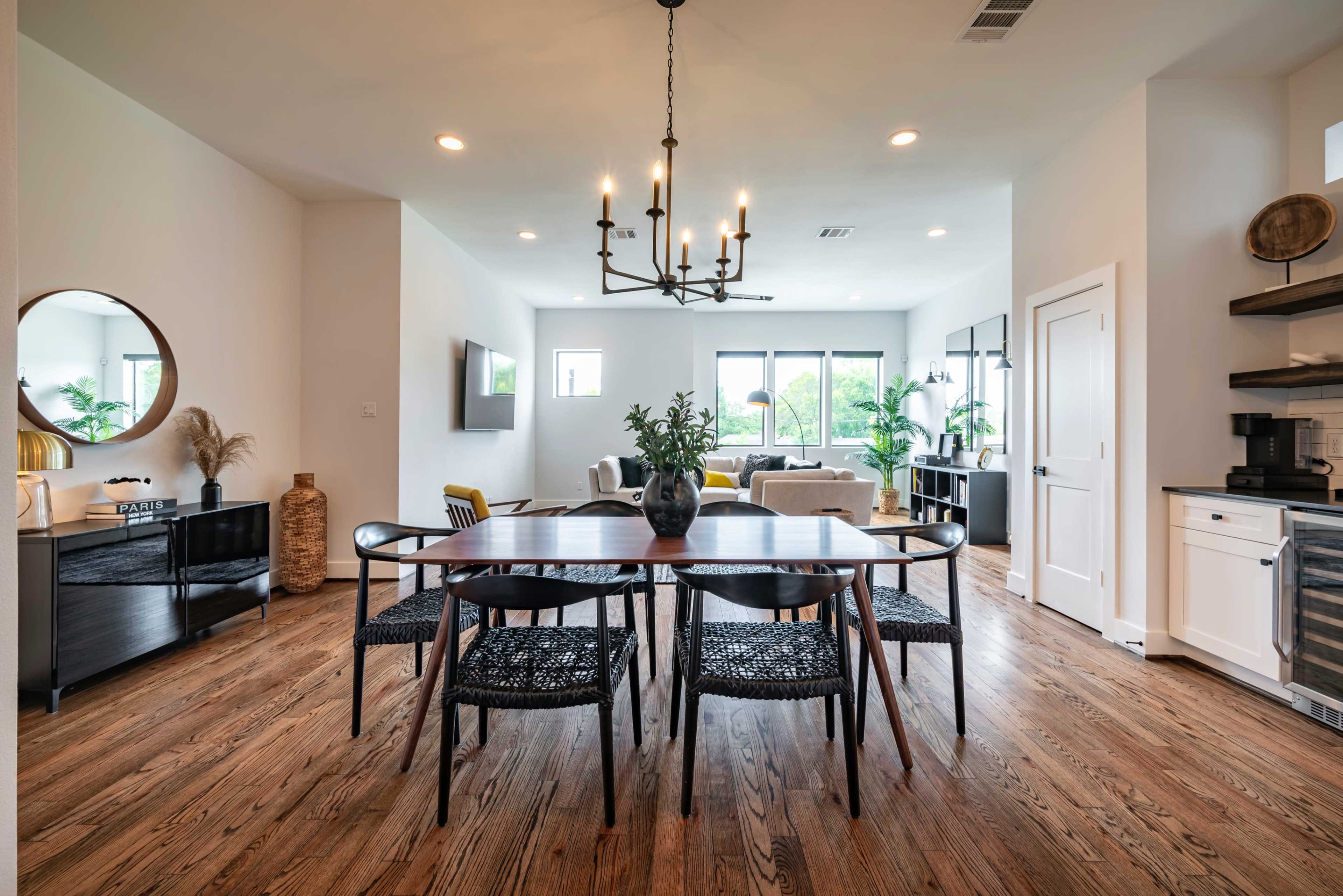 A dining area features a dark wood table surrounded by black chairs, with a modern lighting fixture above and an open layout leading to a living space.