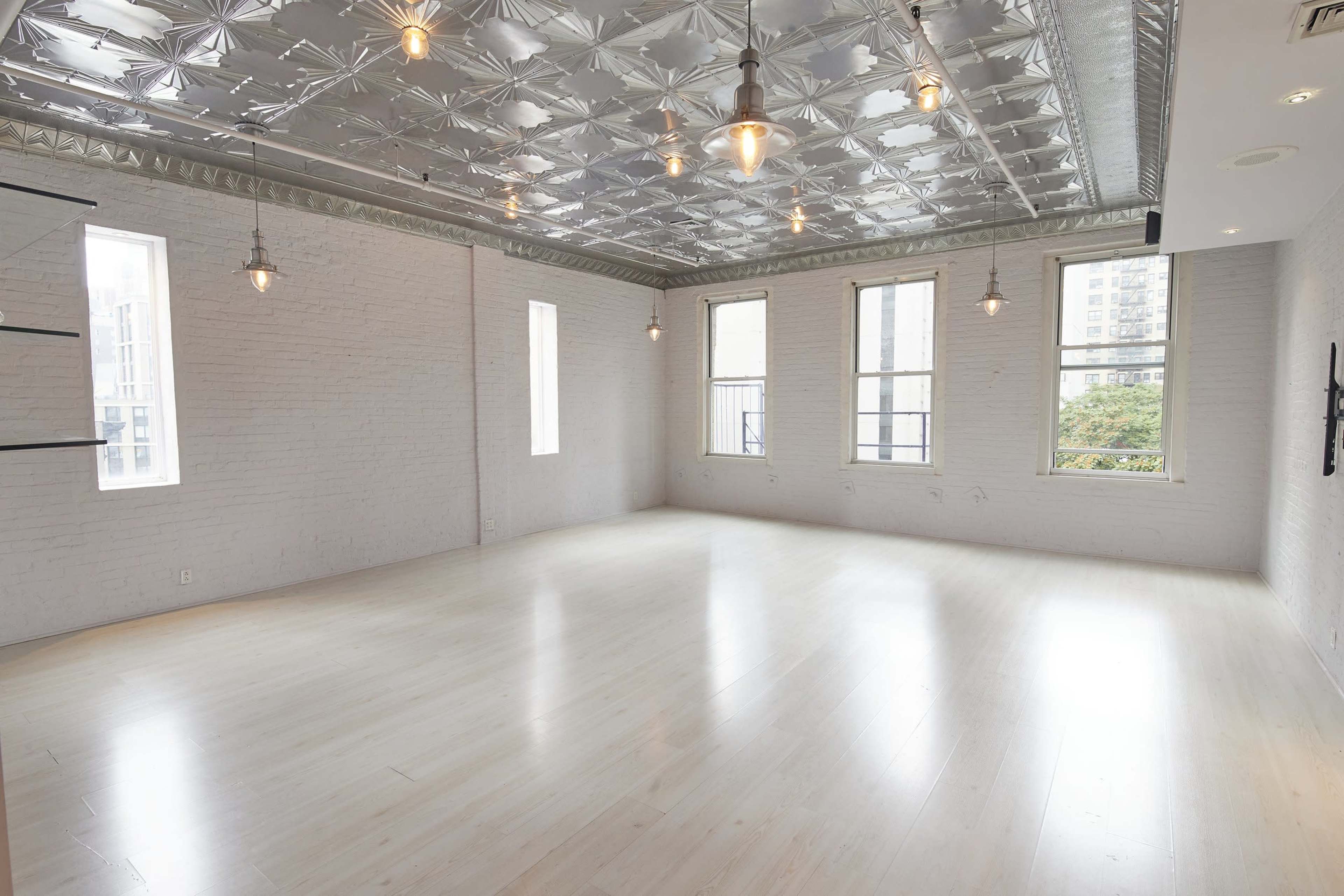 A bright, open room features white brick walls, a silver tin ceiling, and large windows.