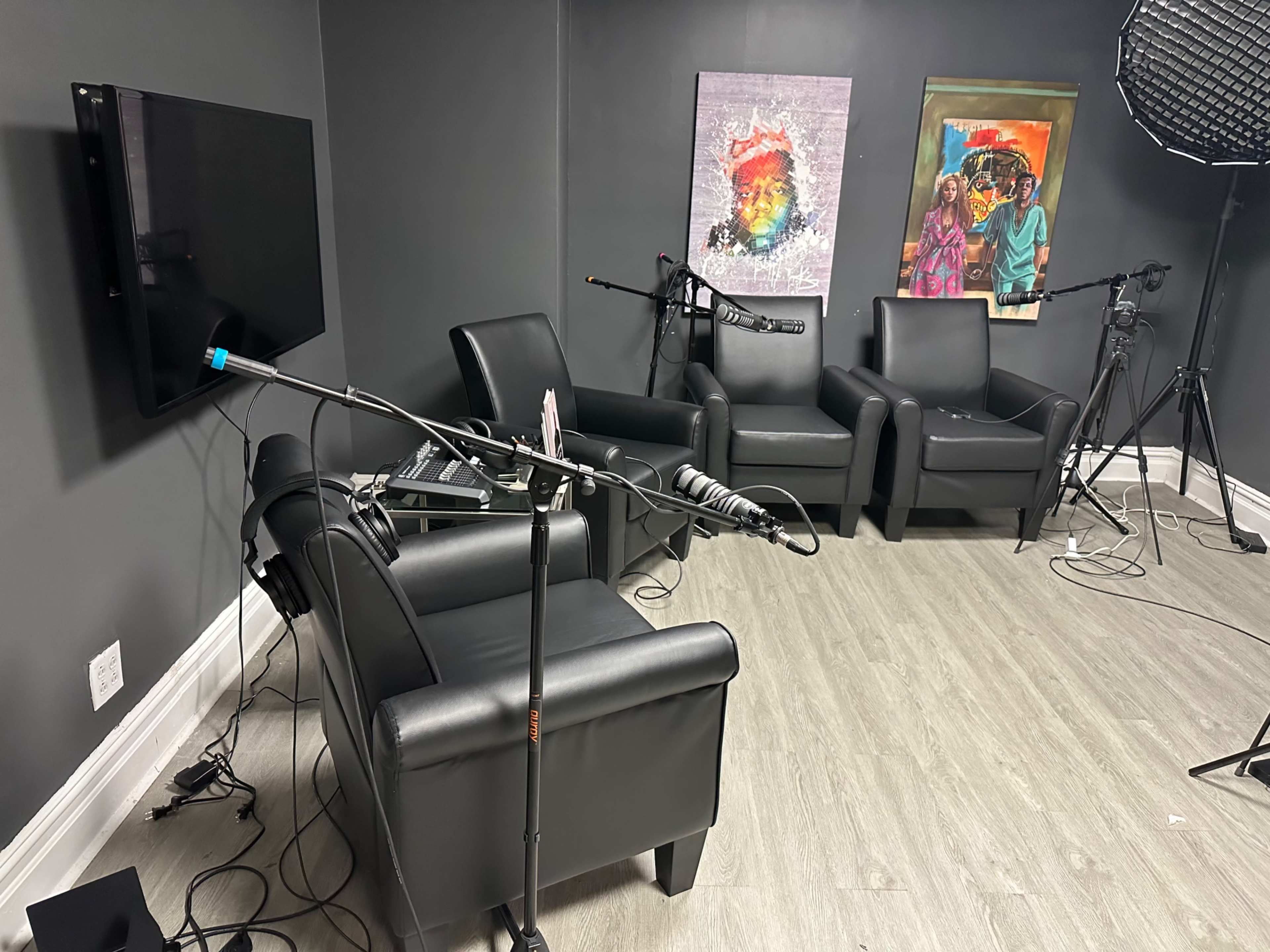 A recording studio setup with black leather chairs, microphones on stands, and colorful artwork on the walls.