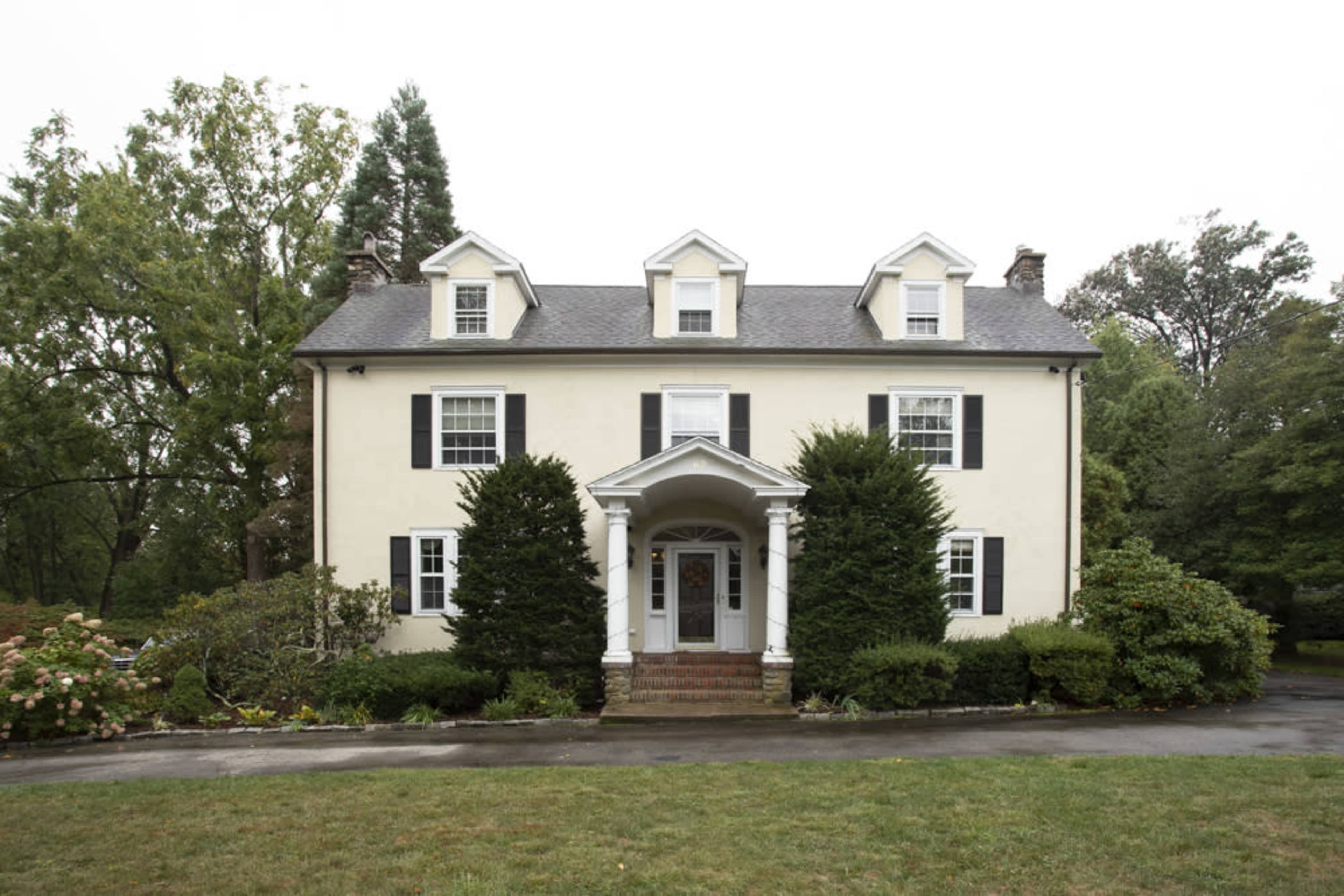 A two-story, colonial-style house with a symmetrical facade, featuring white siding, black shutters, and a front porch supported by columns.