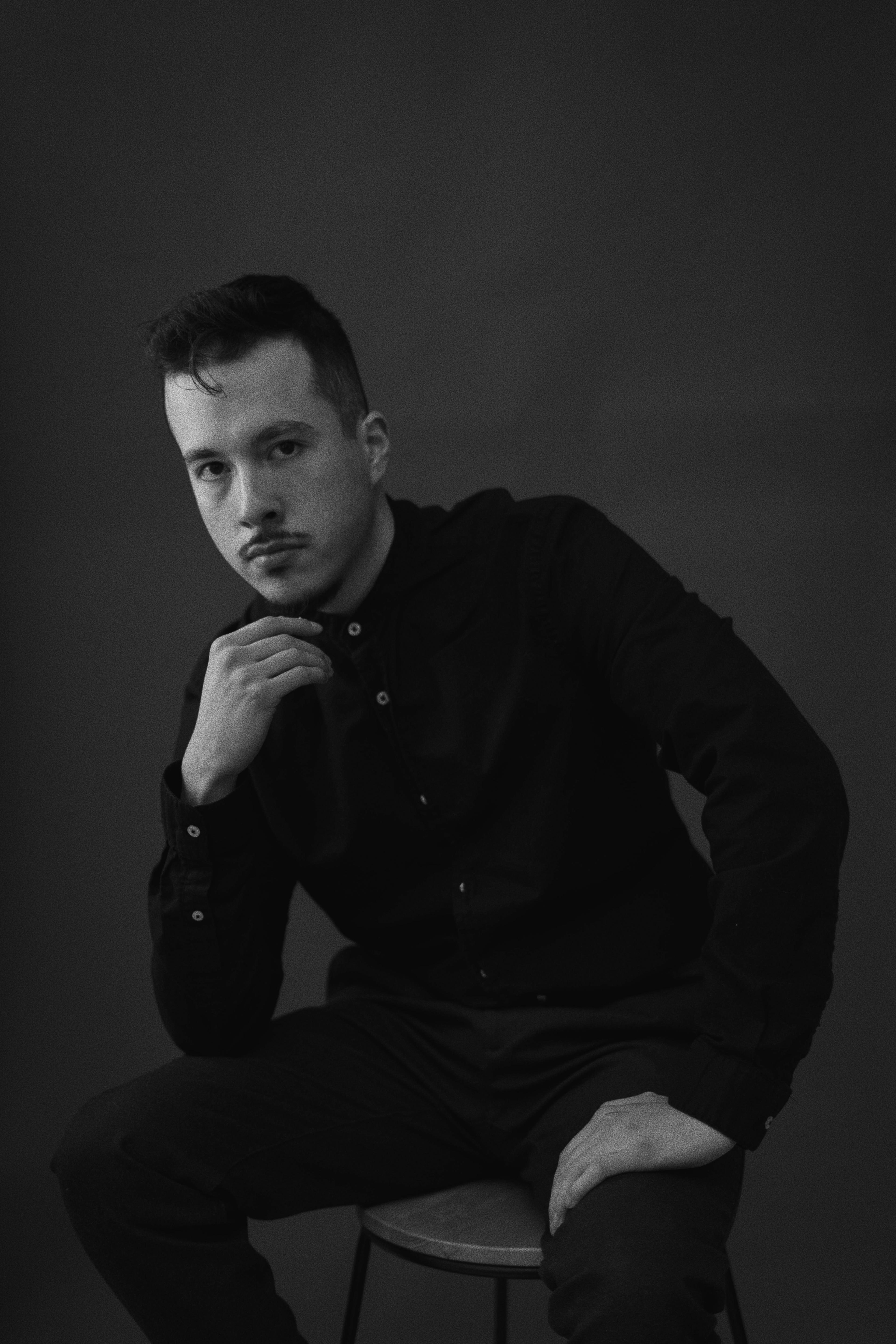 A black and white portrait of a man sitting on a stool.