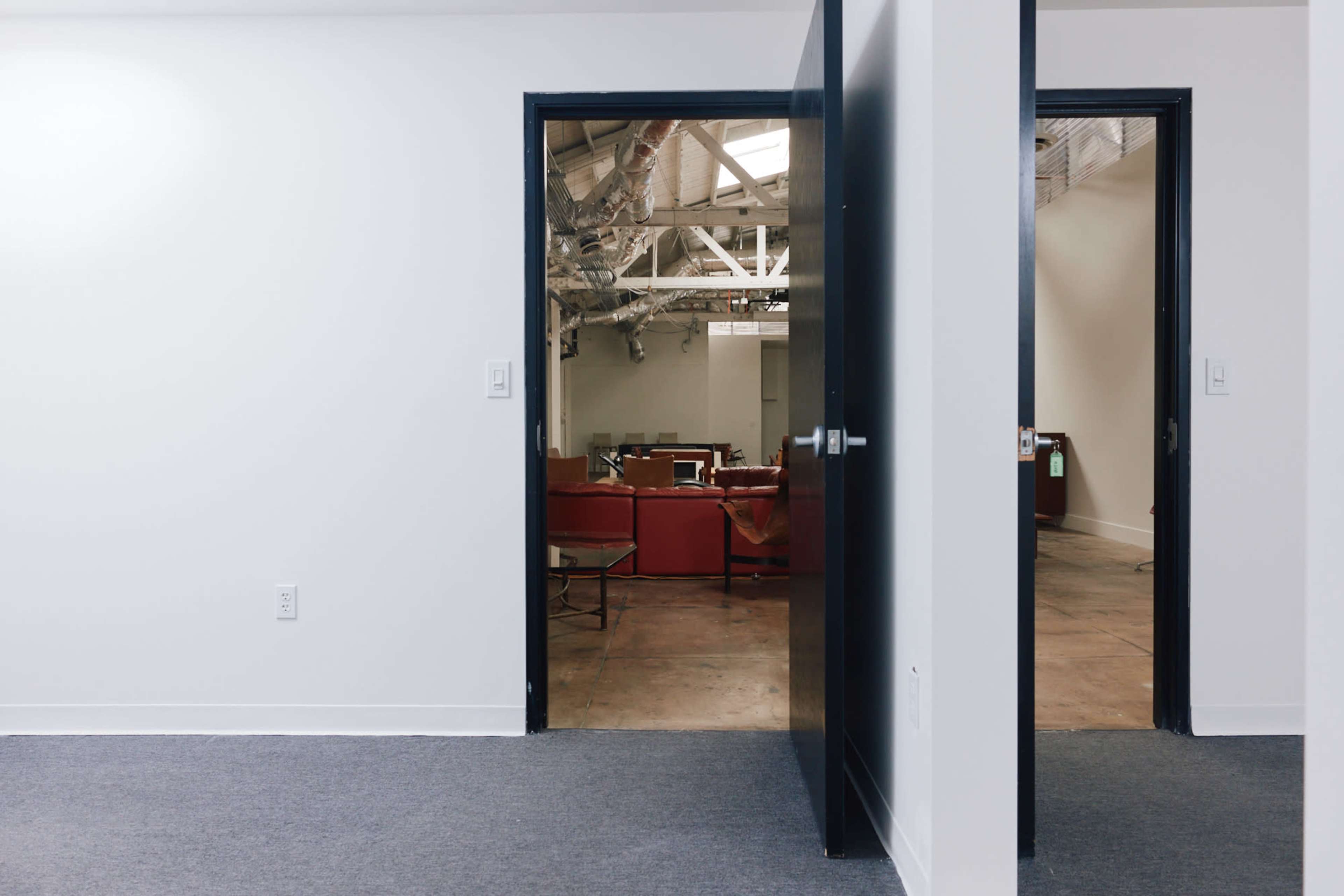 A pair of open doors leads to a room with red furniture and industrial-style ceilings.