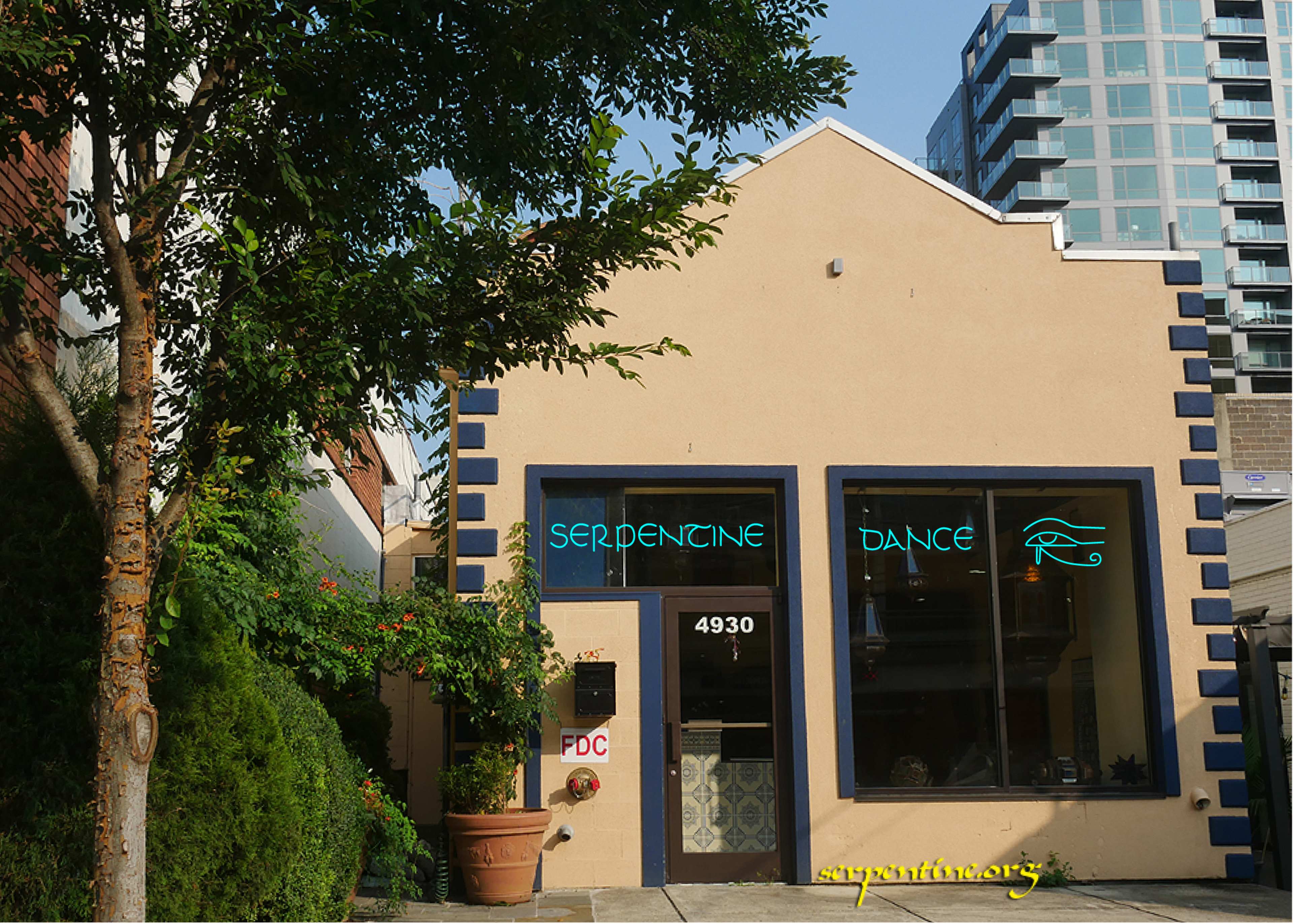 The image shows a beige building with blue trim, featuring large windows and neon signs displaying the words "Serpentine Dance" and an eye symbol.