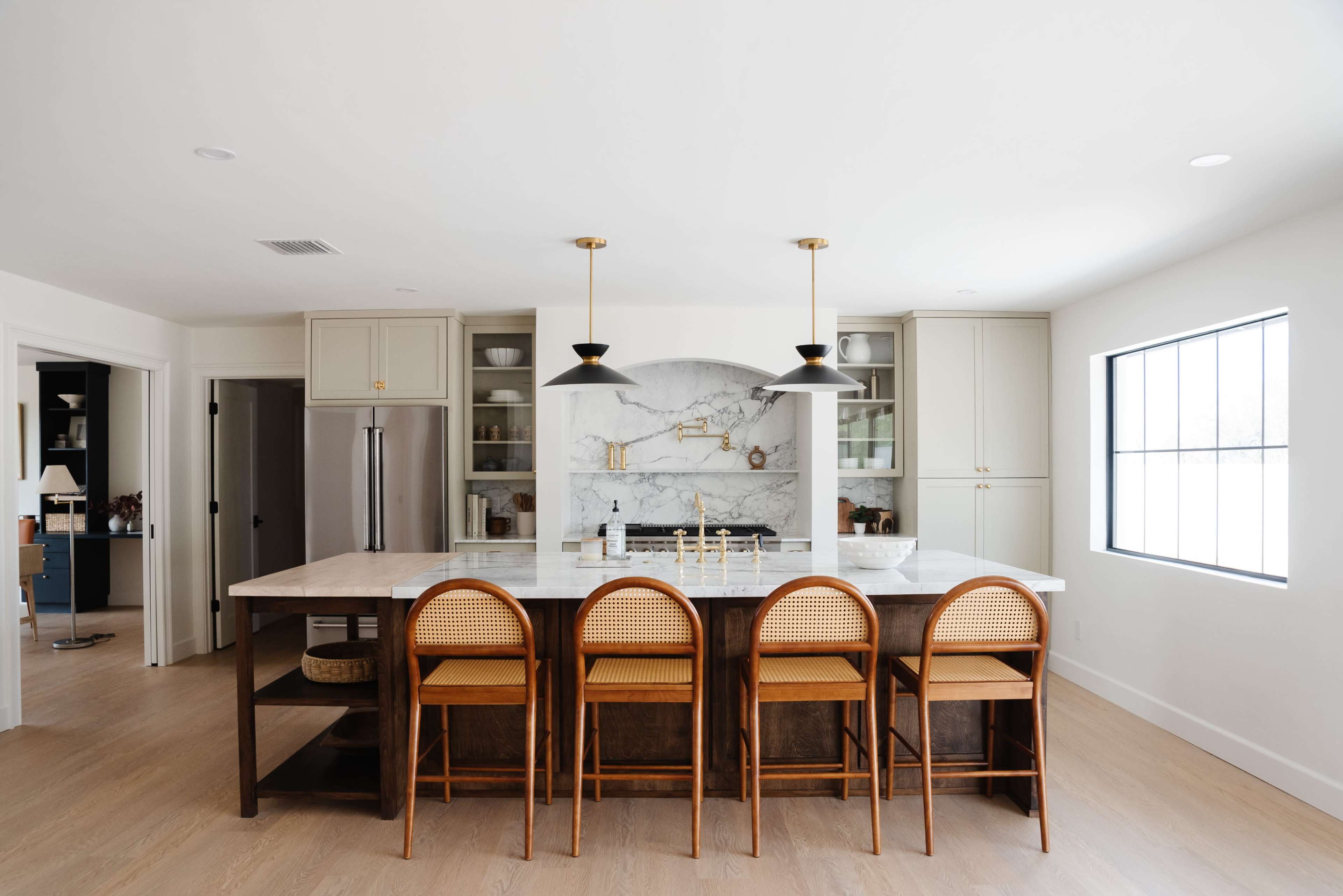 A modern kitchen features a marble countertop island with four wooden stools and stylish light fixtures above, surrounded by cabinetry and a marble backsplash.