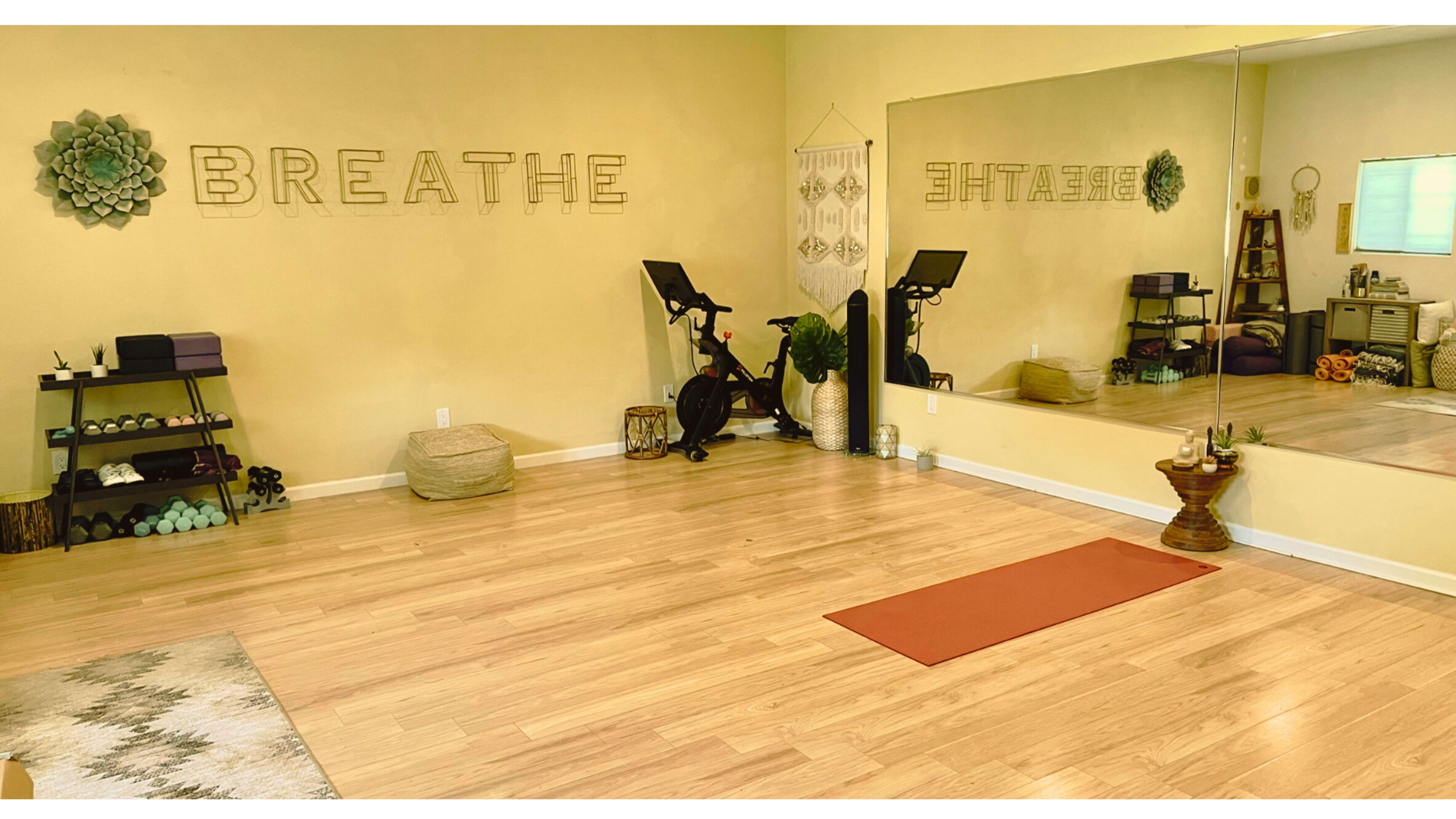A yoga studio with a mirrored wall, exercise equipment, a yoga mat, and decorative elements.