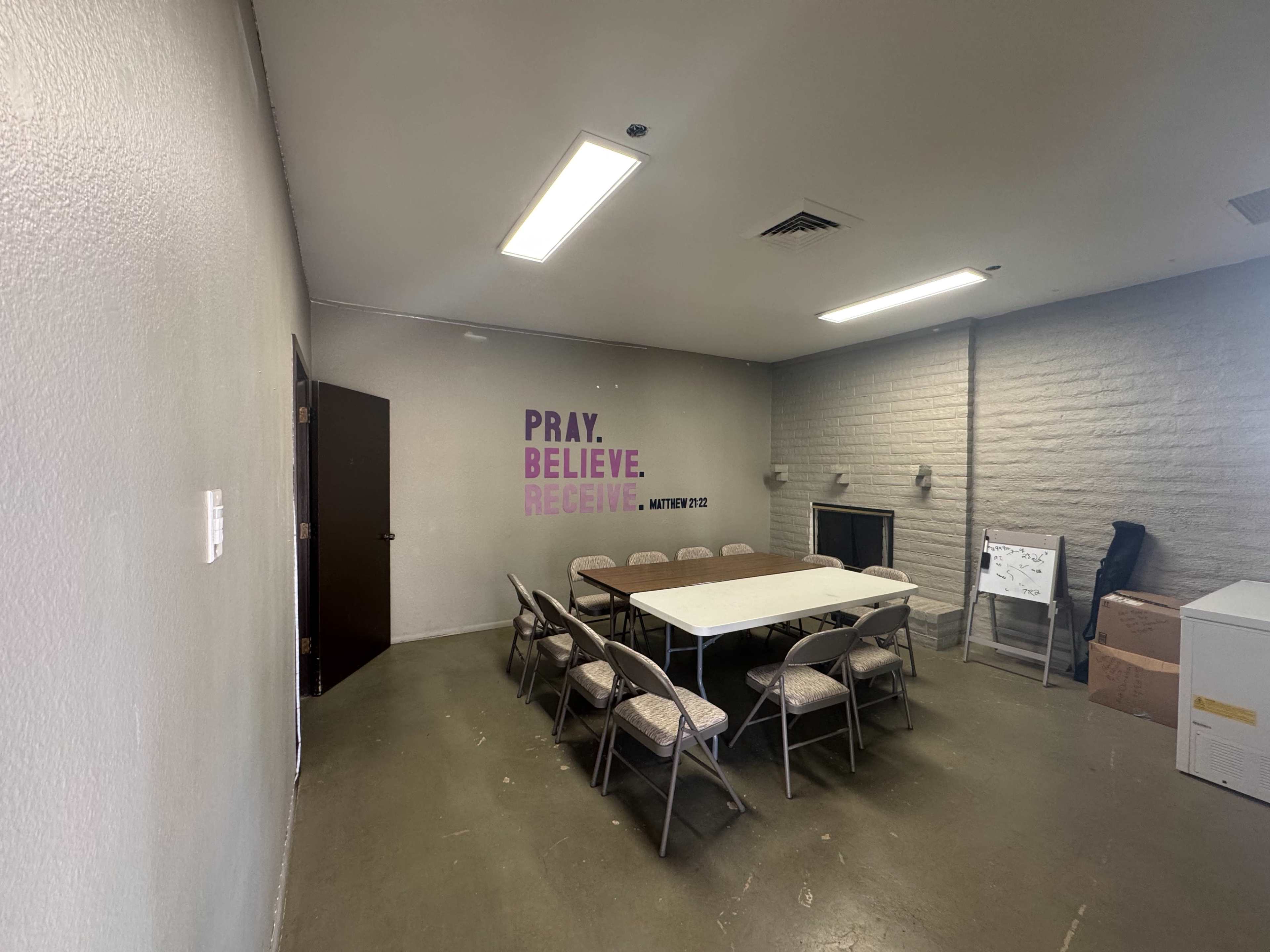 A meeting room features a large table surrounded by chairs, with a motivational phrase displayed on the wall.