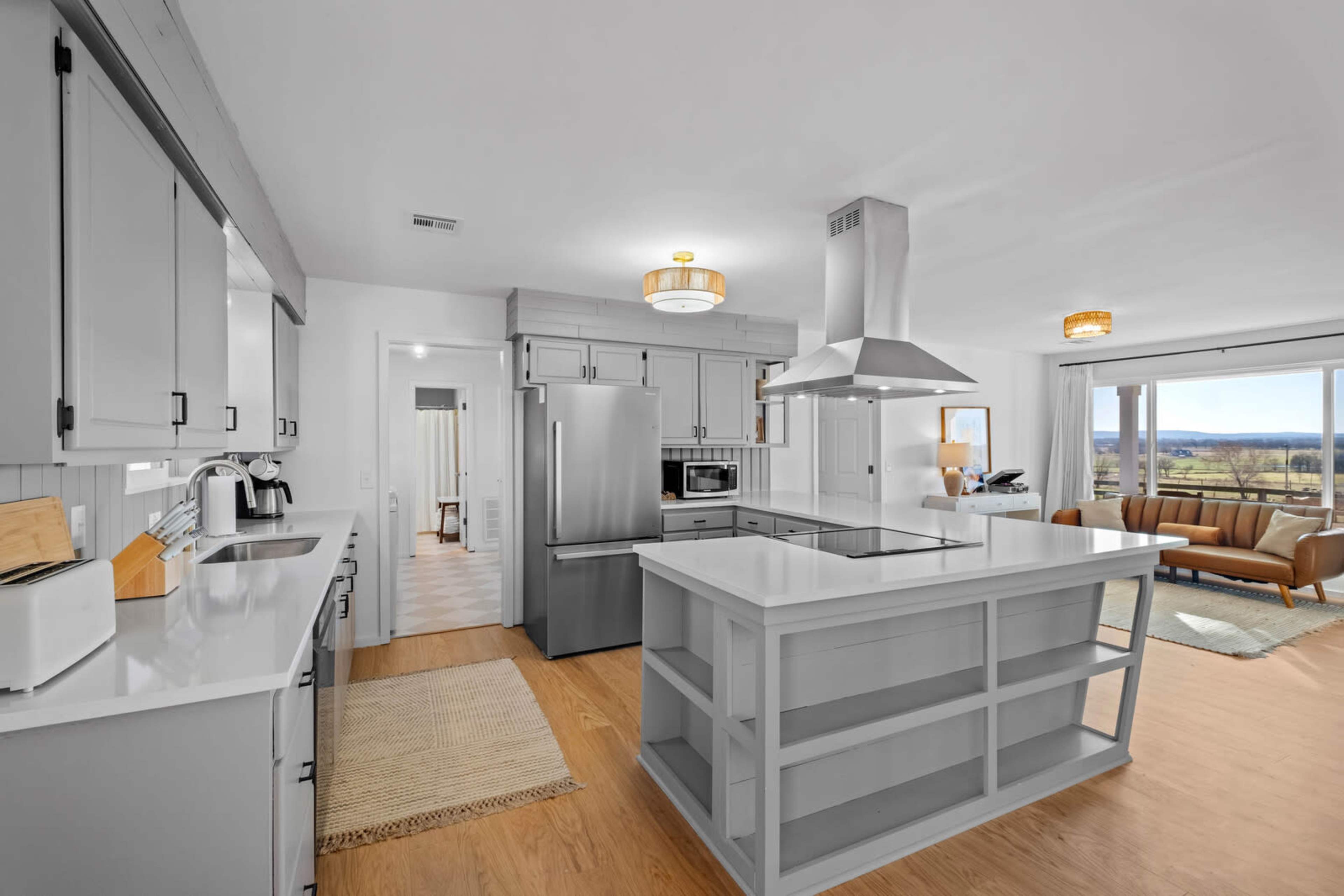 A modern kitchen features gray cabinetry, stainless steel appliances, and an island with a cooktop, complemented by large windows showcasing a scenic view.