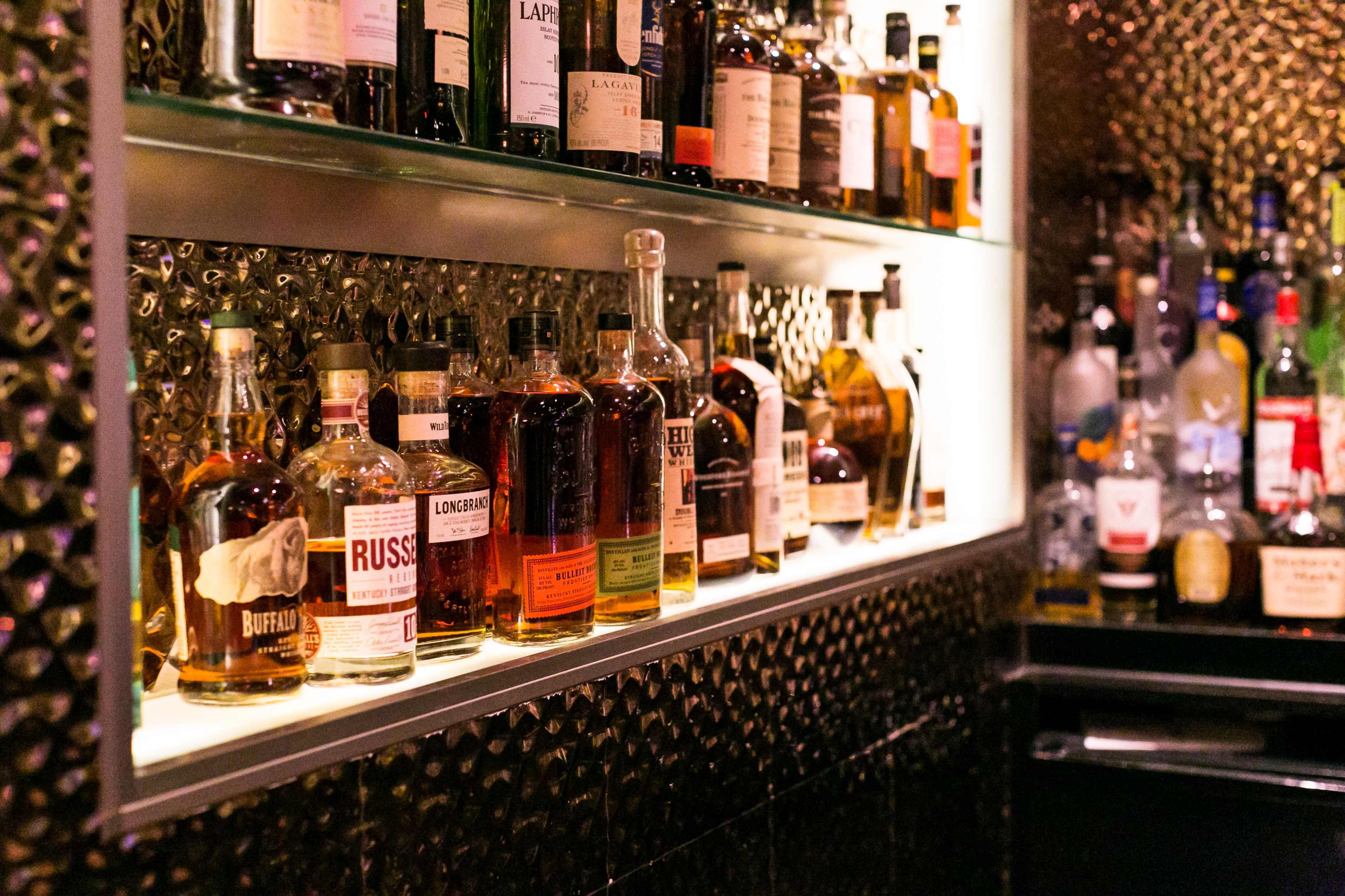 A backlit shelf filled with various bottles of whiskey and other spirits.