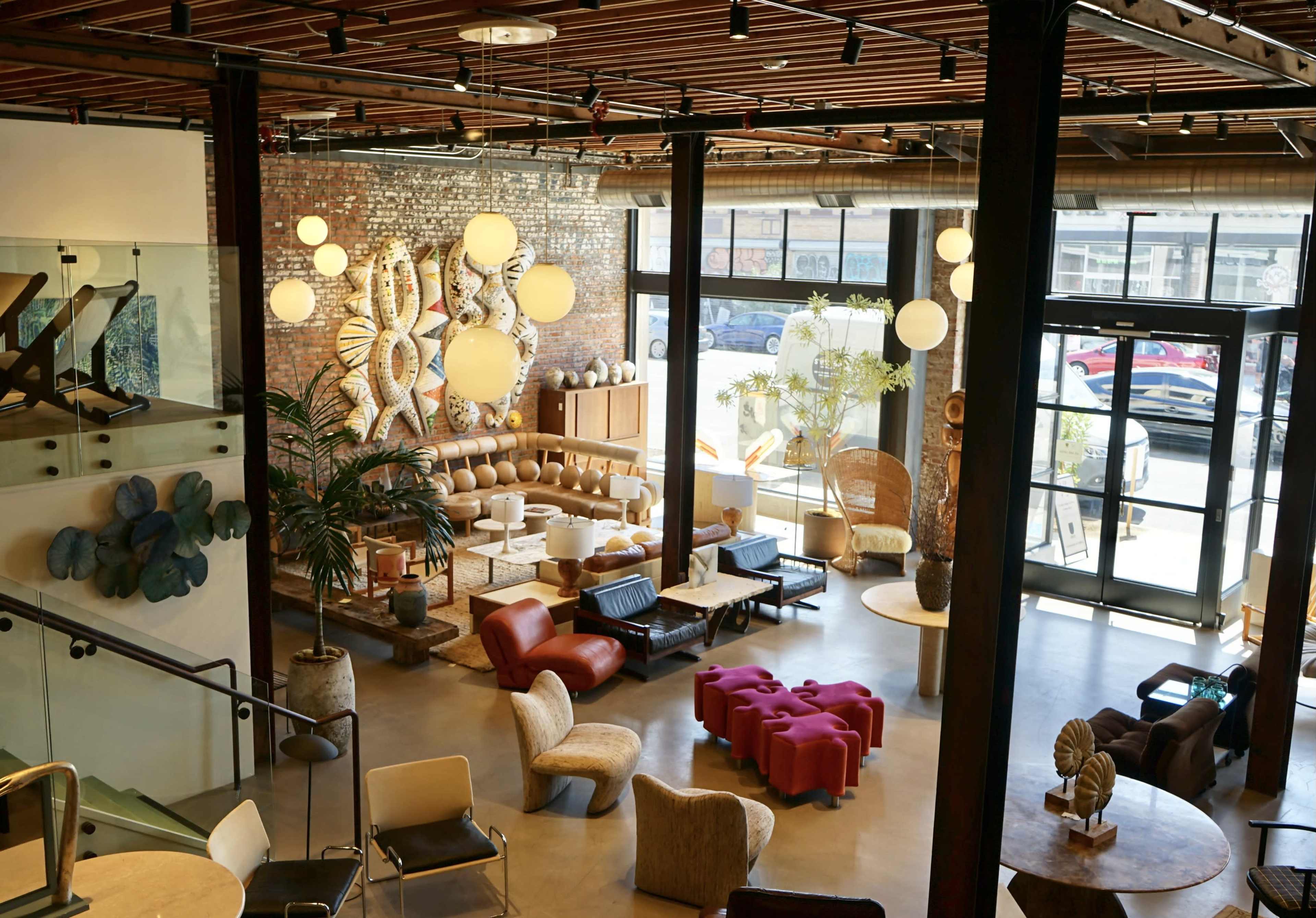 A modern, open space filled with various seating arrangements, decorative elements, and large windows allowing natural light to enter.