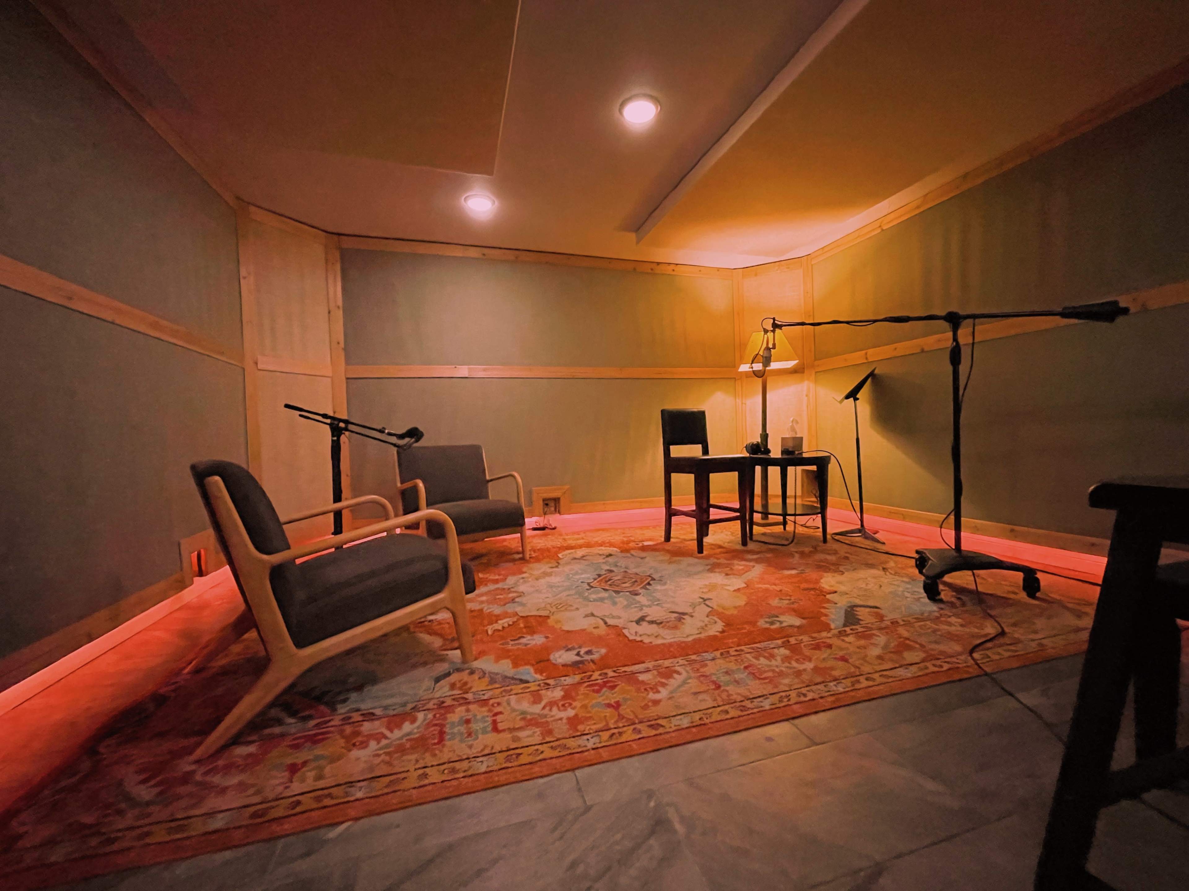 A small recording studio with two chairs, a table, a microphone setup, and warm lighting.