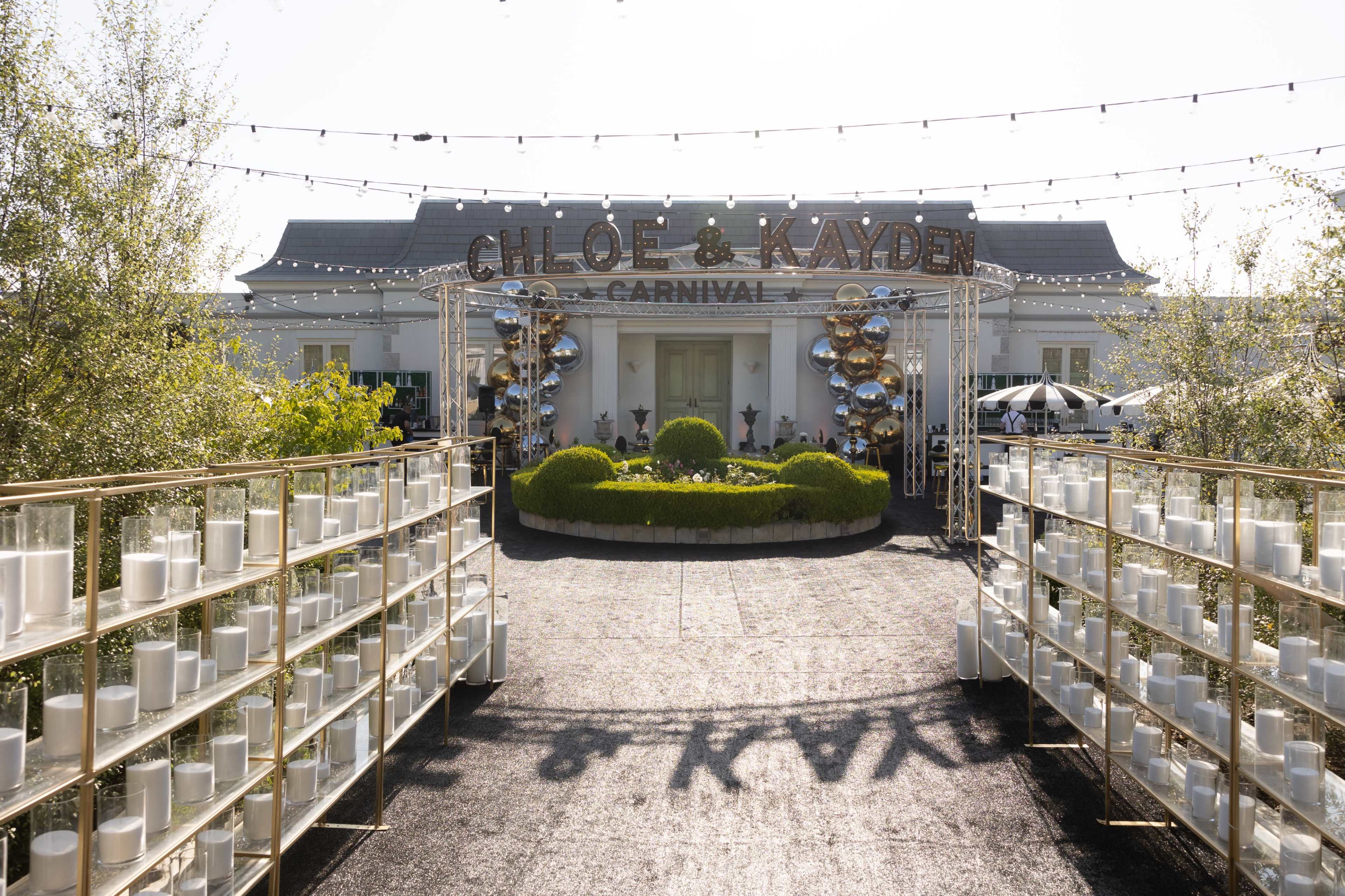 A path lined with white candles leads to a building adorned with a sign that reads "Chloe & Kayden Carnival."