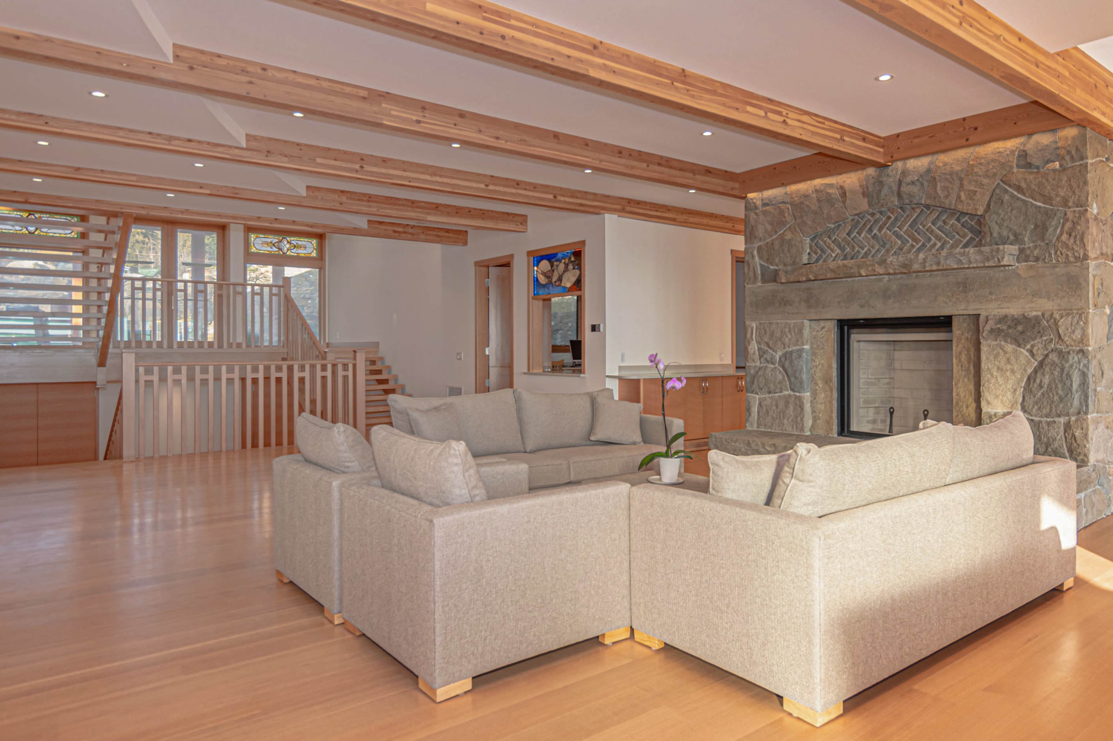 A spacious living room with a stone fireplace, wooden beam ceiling, and a light-colored sectional sofa arranged around a central coffee table.