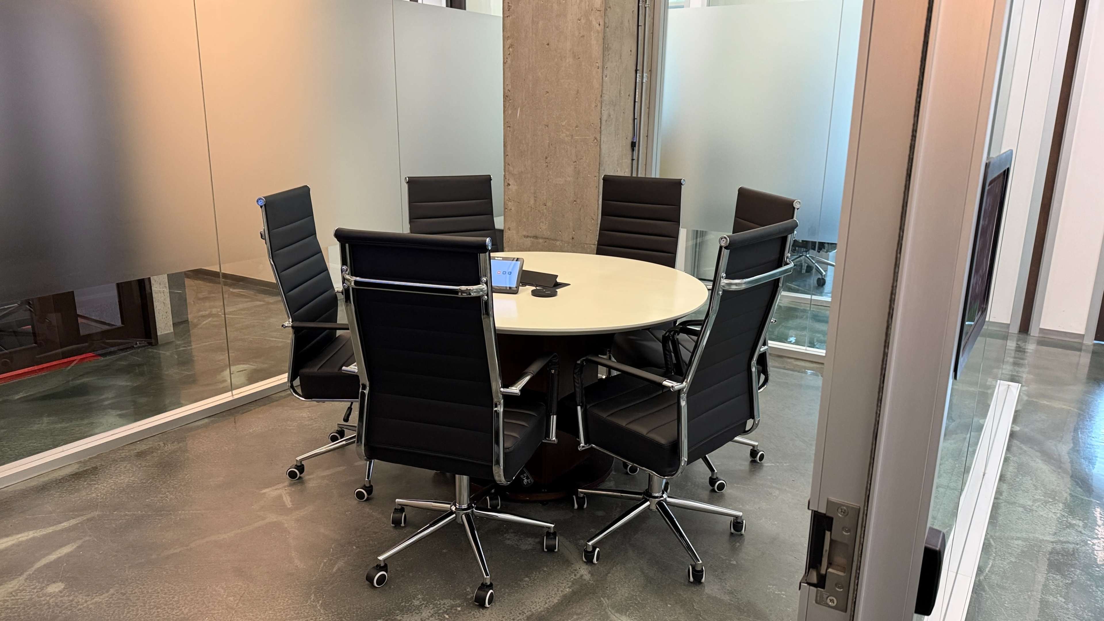 The image shows a modern conference room with a round table surrounded by eight black ergonomic chairs.