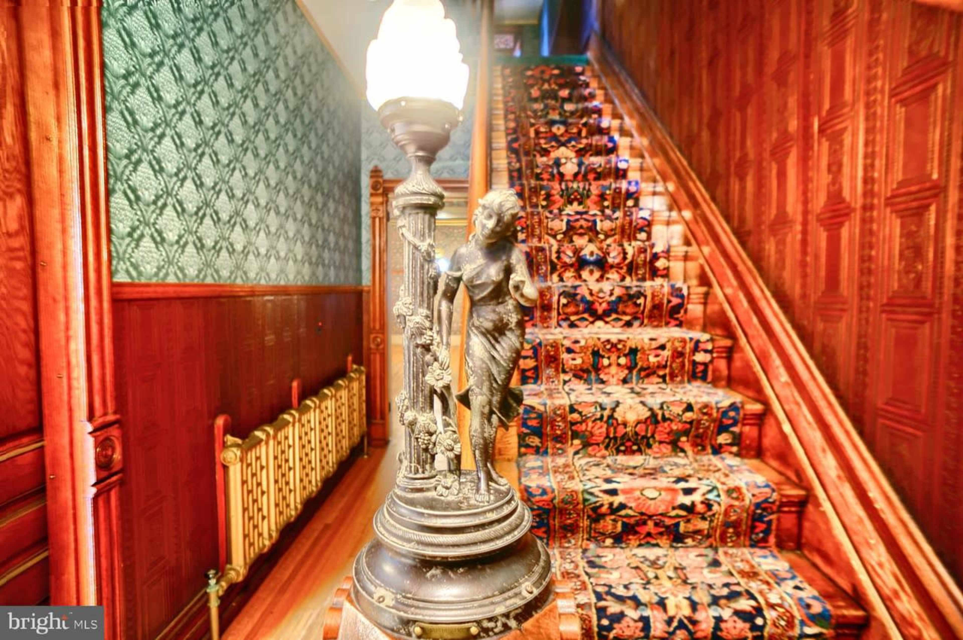 A decorative lamp featuring a statue stands beside a carpeted staircase with ornate patterns and wooden paneling on the walls.