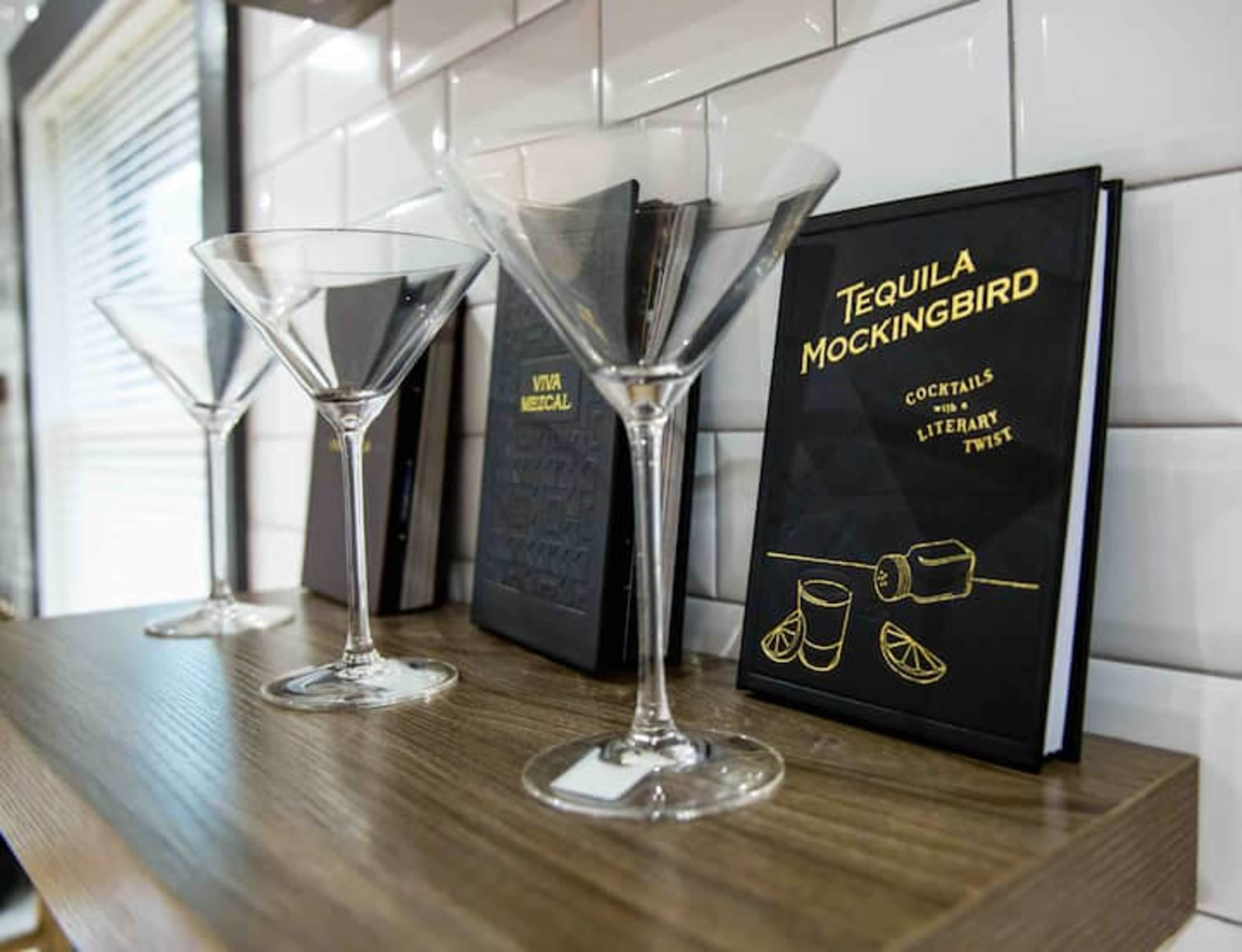 A shelf displays a cookbook titled "Tequila Mockingbird" alongside three empty martini glasses.
