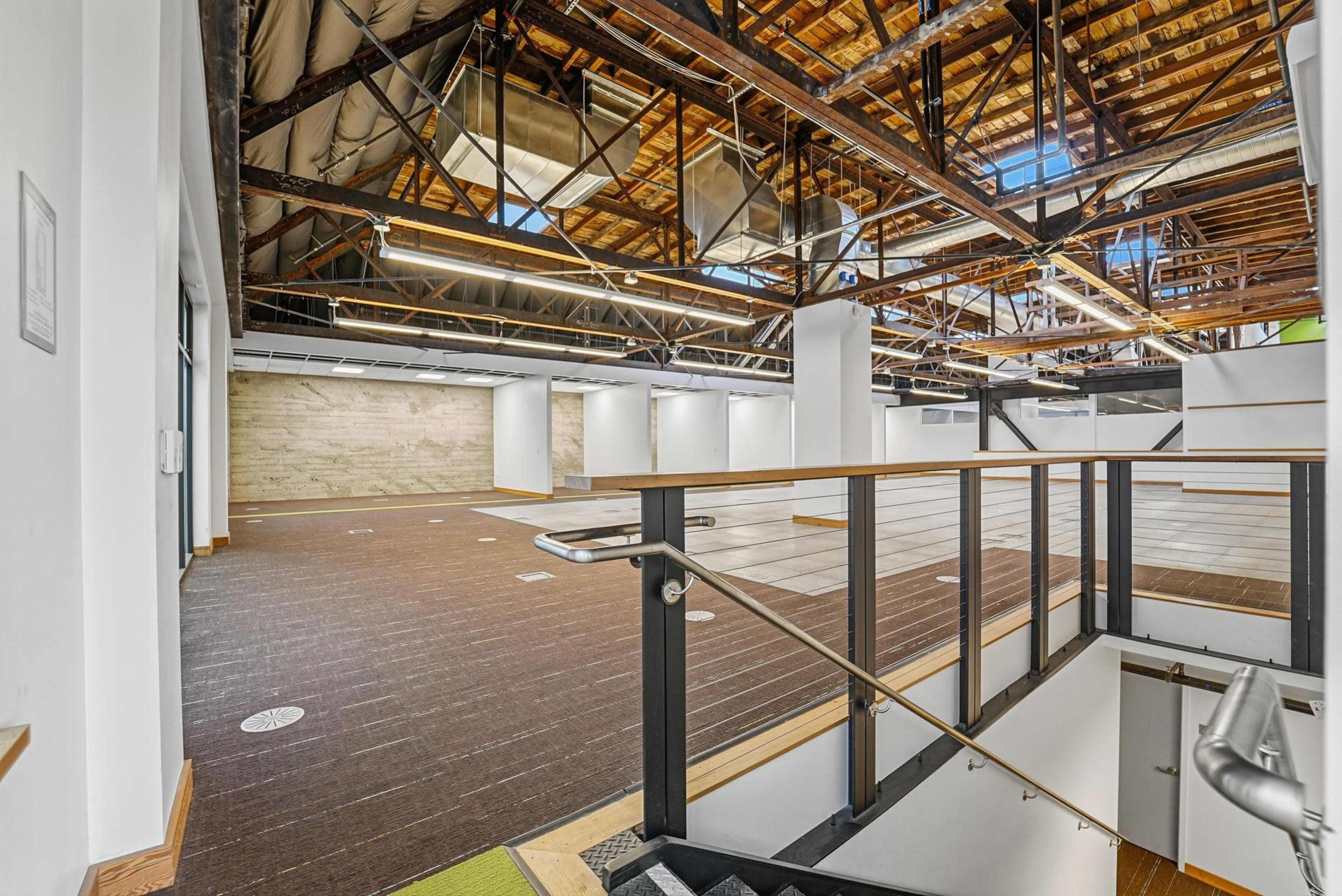 The image shows a spacious, modern interior with wooden beams, open floor layout, and distinct areas for potential use.