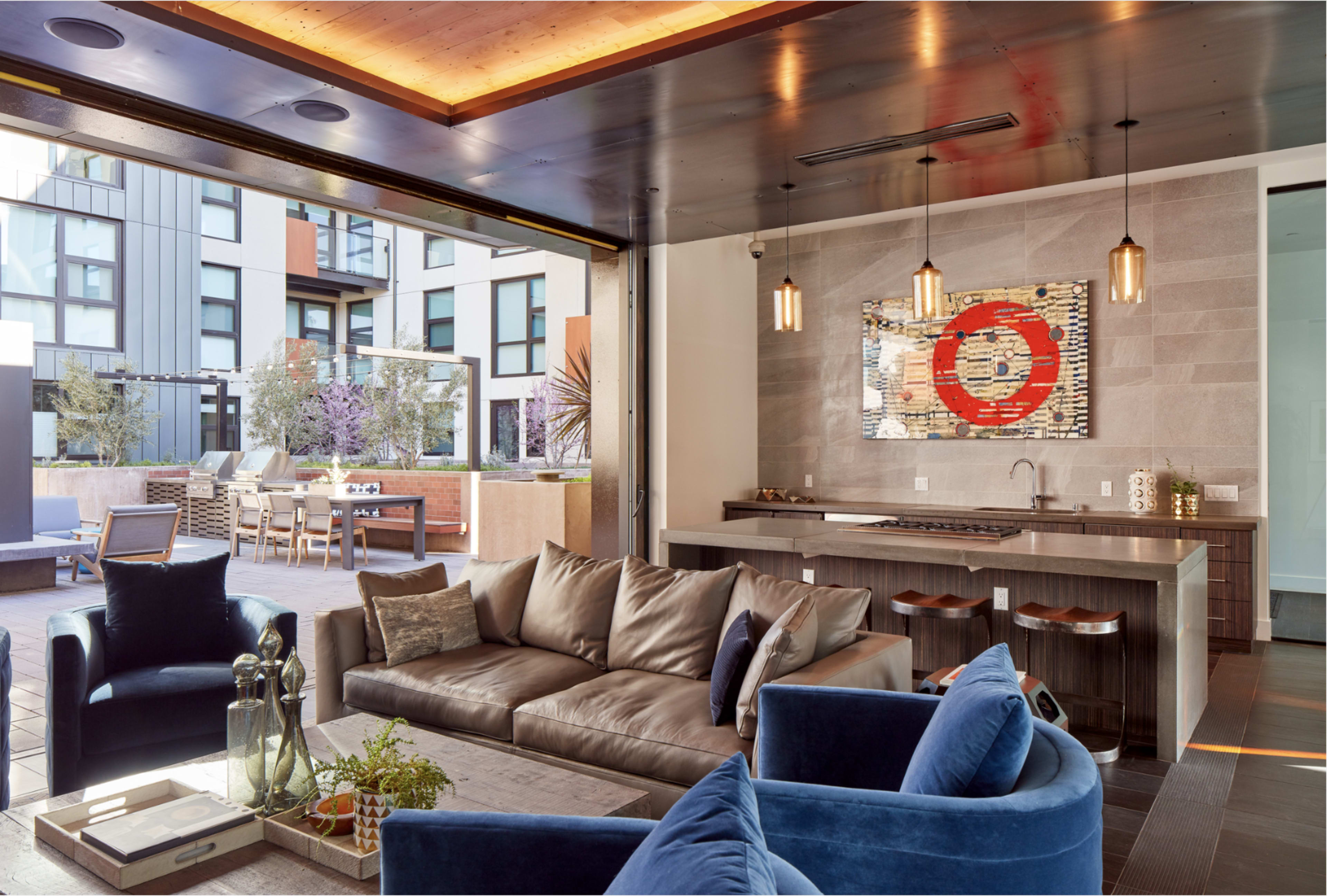 The image features a modern indoor living space that opens up to an outdoor patio, complete with a kitchen area, seating, and stylish decor.