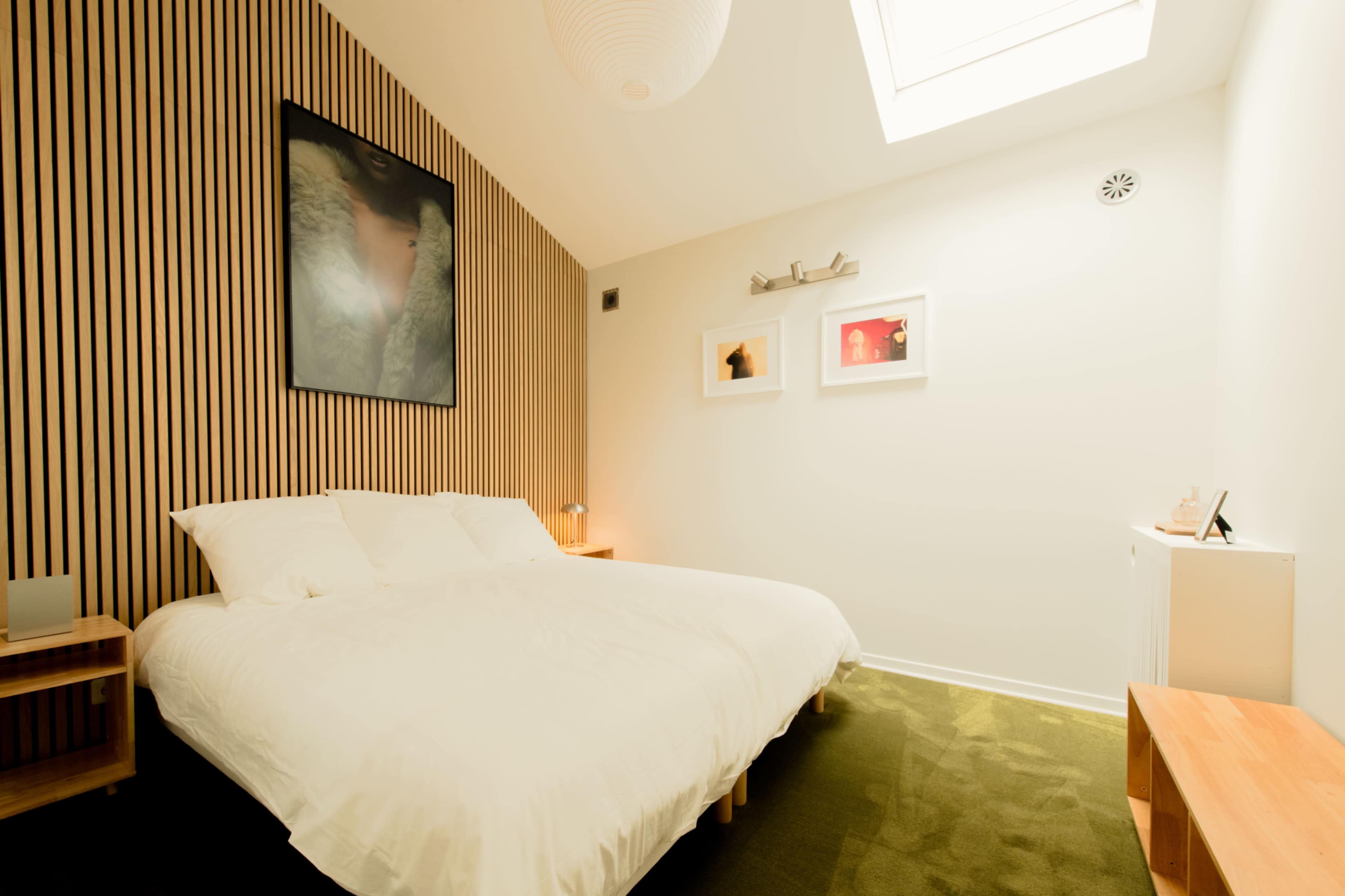 The image shows a modern bedroom with a double bed, wooden accent walls, and ceiling-mounted skylight.
