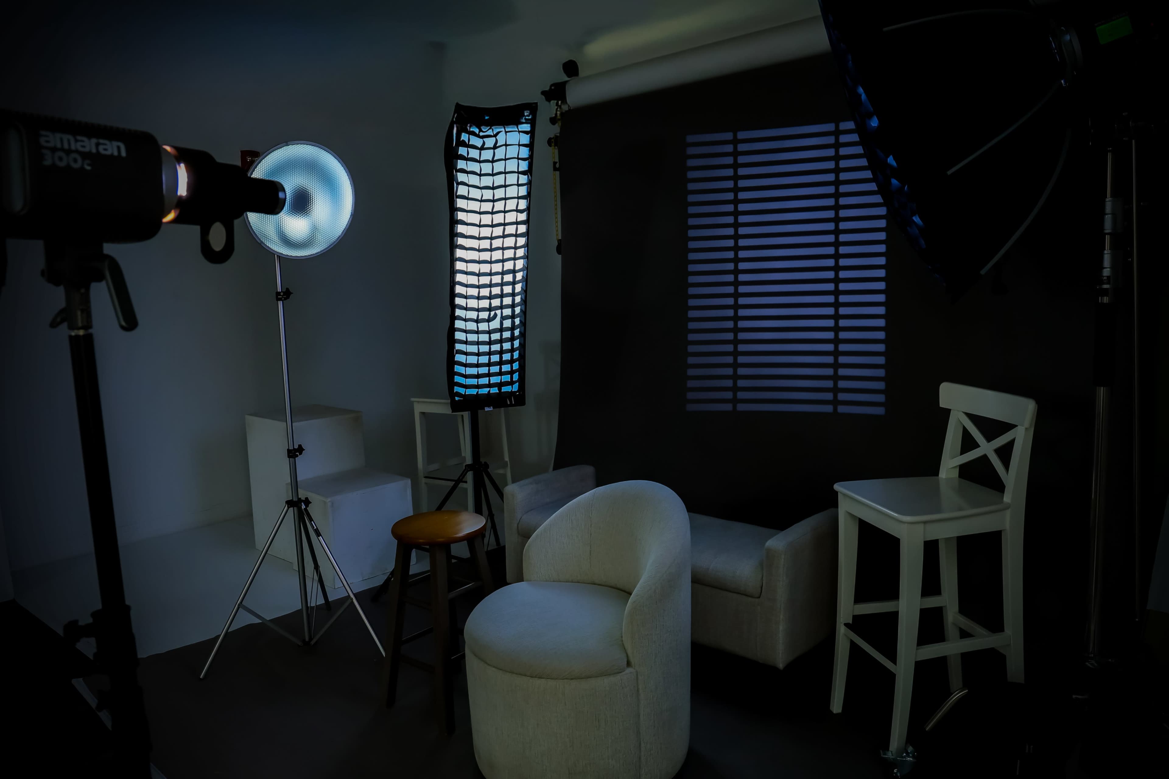 The image shows a photography studio setup with various lighting equipment, a textured backdrop, and a seating arrangement consisting of a chair and a stool.