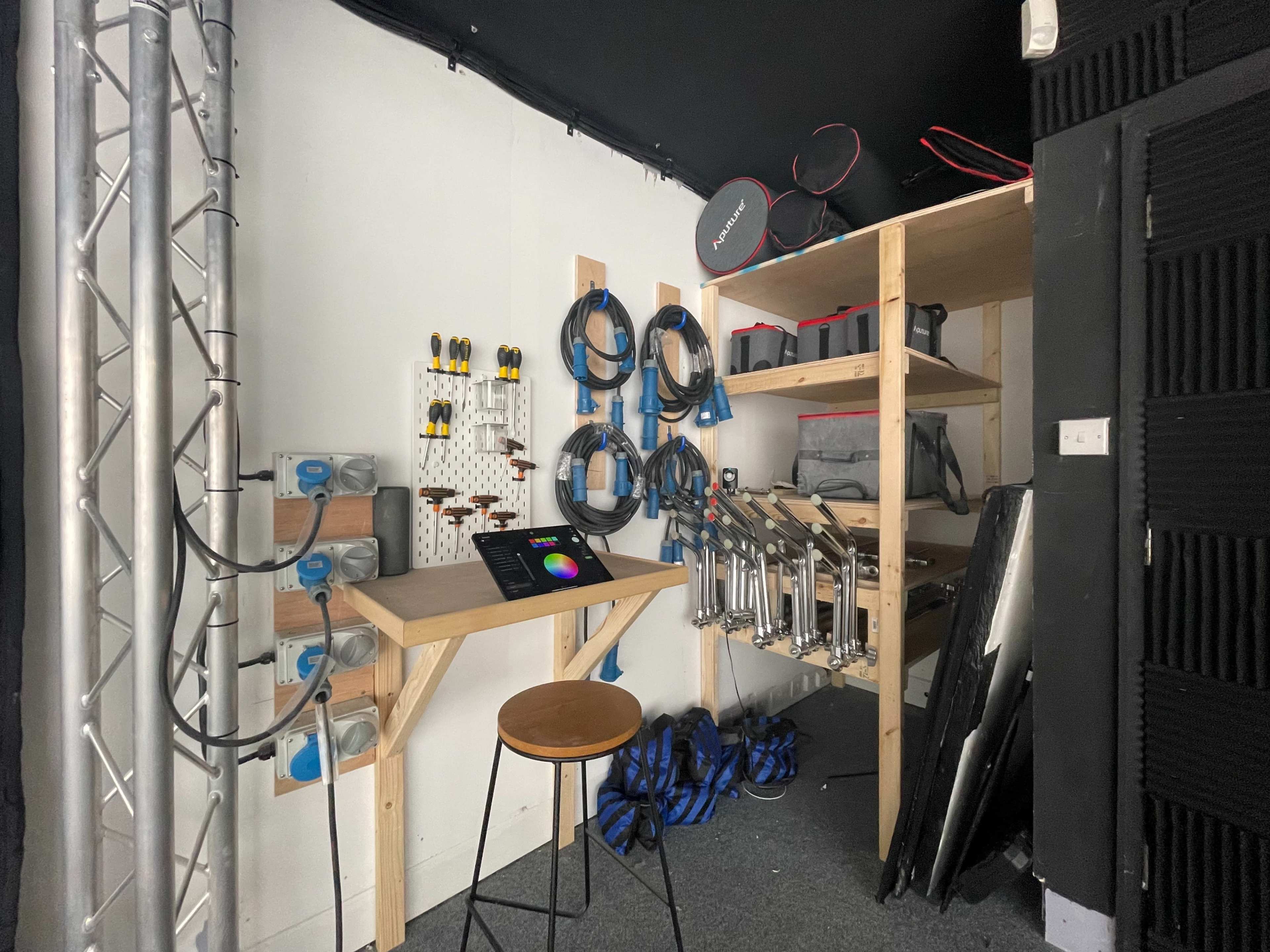A workspace with a wooden table, various cables and tools organized on the walls, and storage shelves containing equipment.