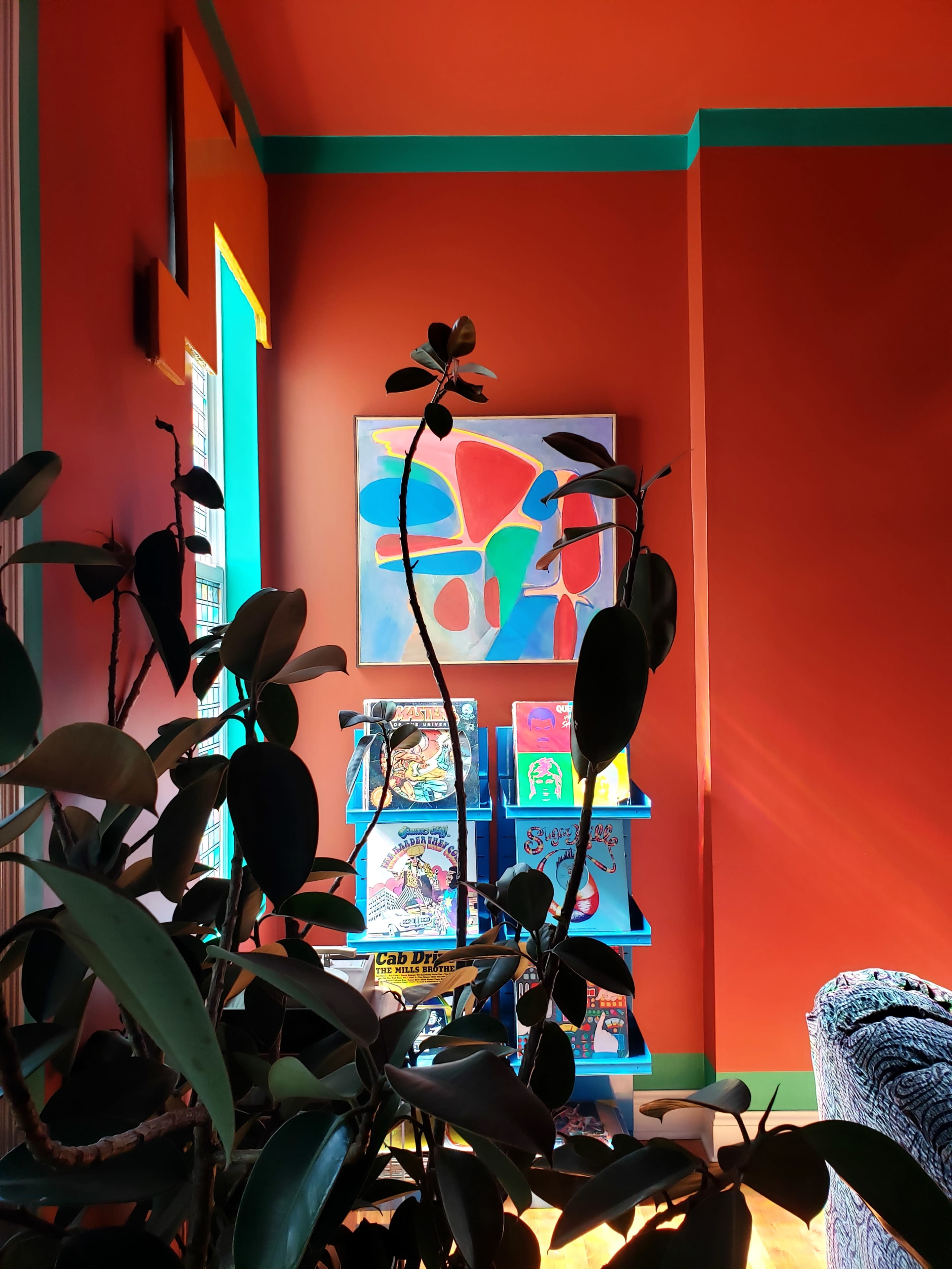 A brightly colored room features a painting on the wall and a bookshelf filled with various books, framed by green and orange accents.