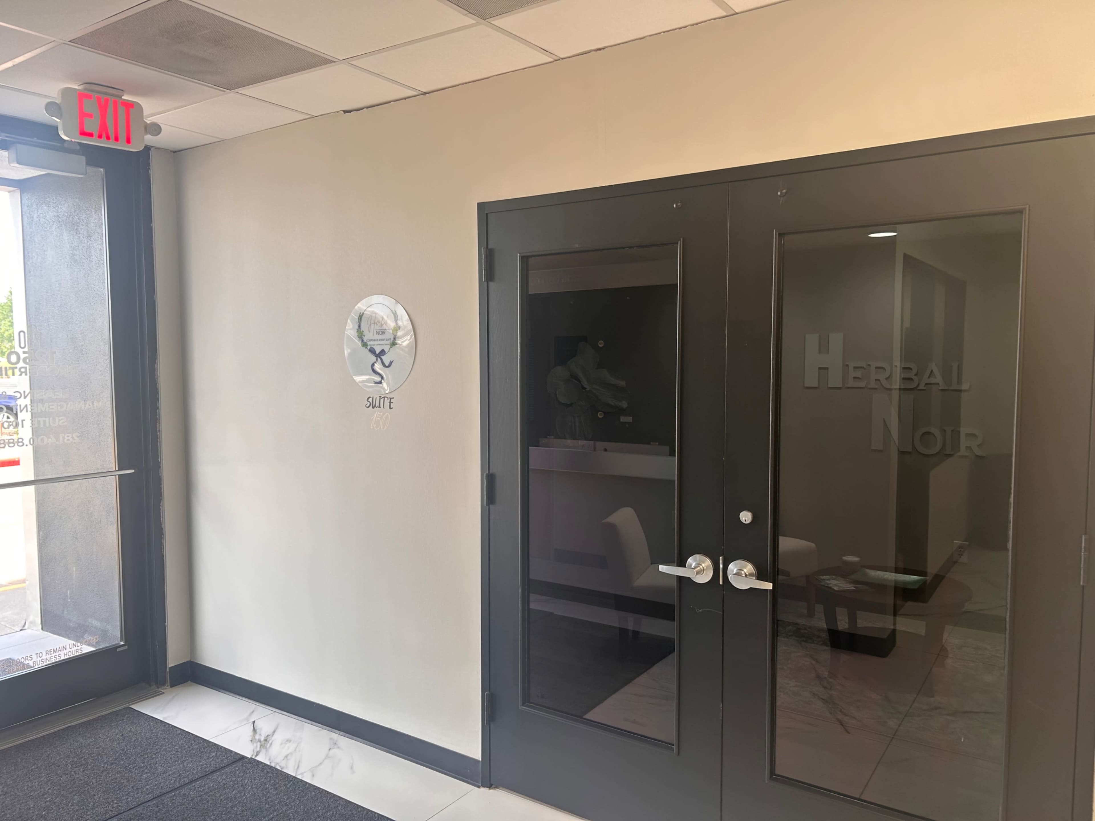 The image shows a modern entryway with glass doors labeled "HERBAL NOIR" and a sign for "SUITE 420" on the wall.