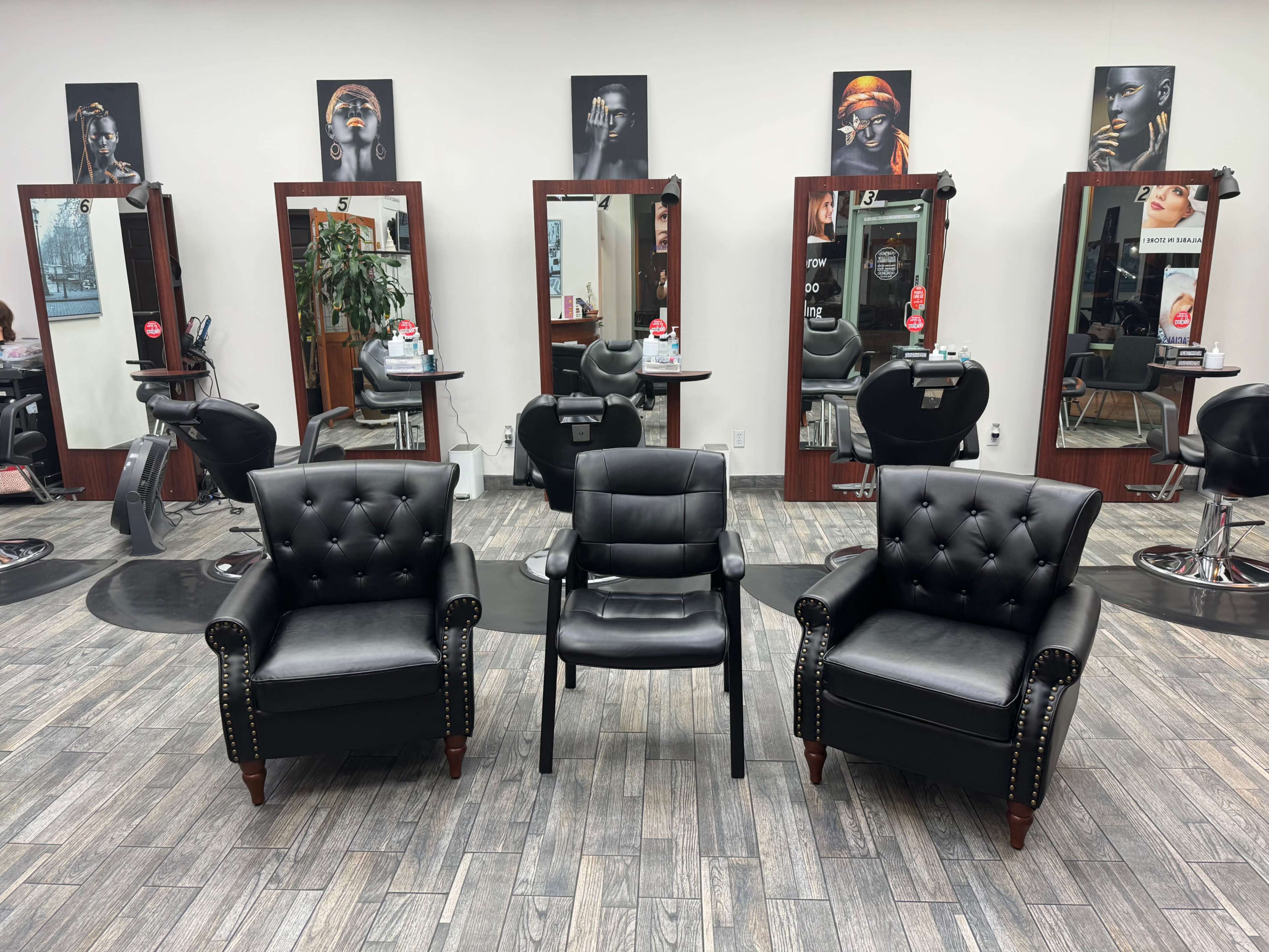 The image shows a hair salon featuring three black chairs in the foreground and several mirrors with stylist stations in the background.
