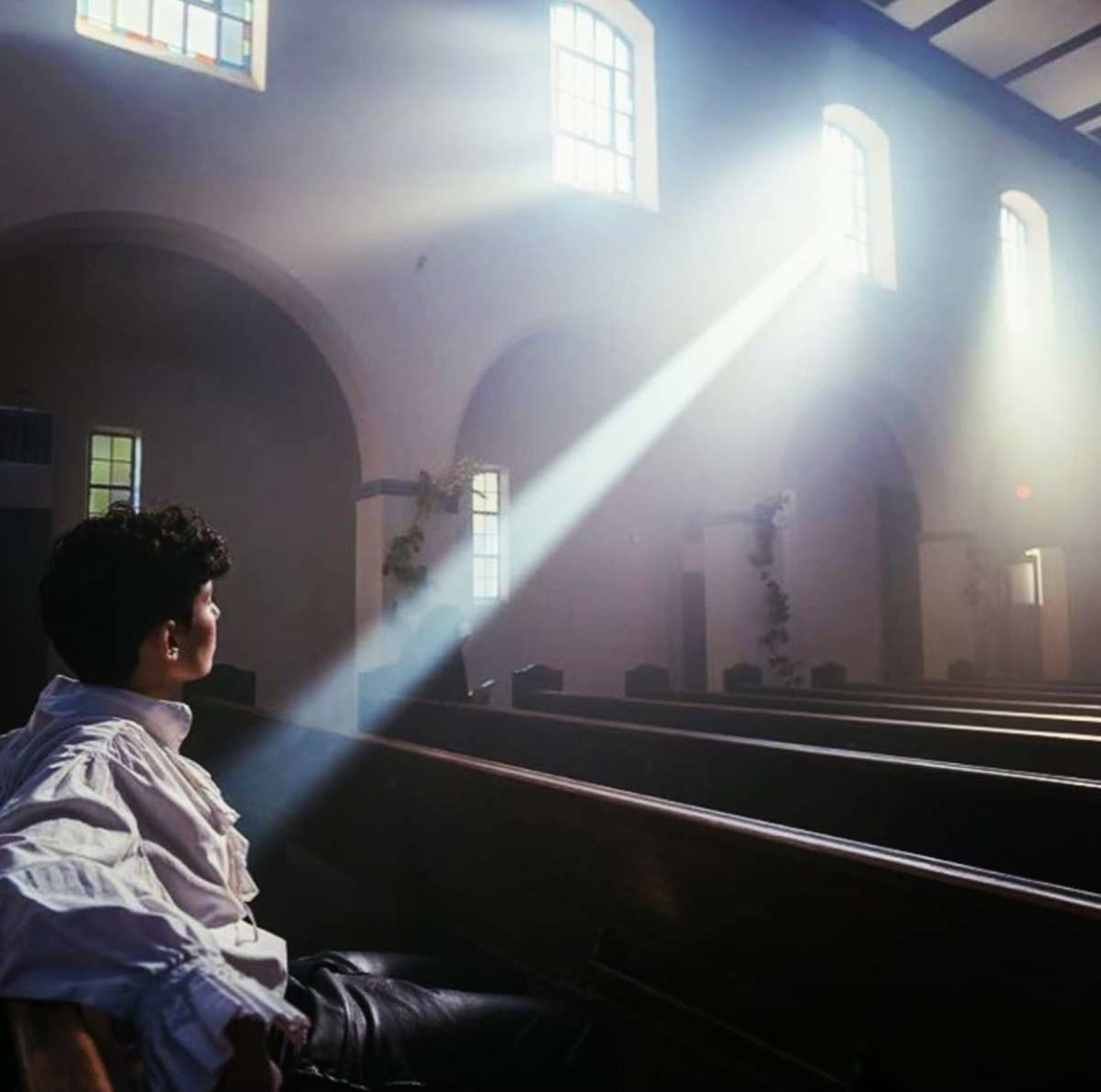 A person sits in a church, illuminated by a beam of sunlight streaming through a window.