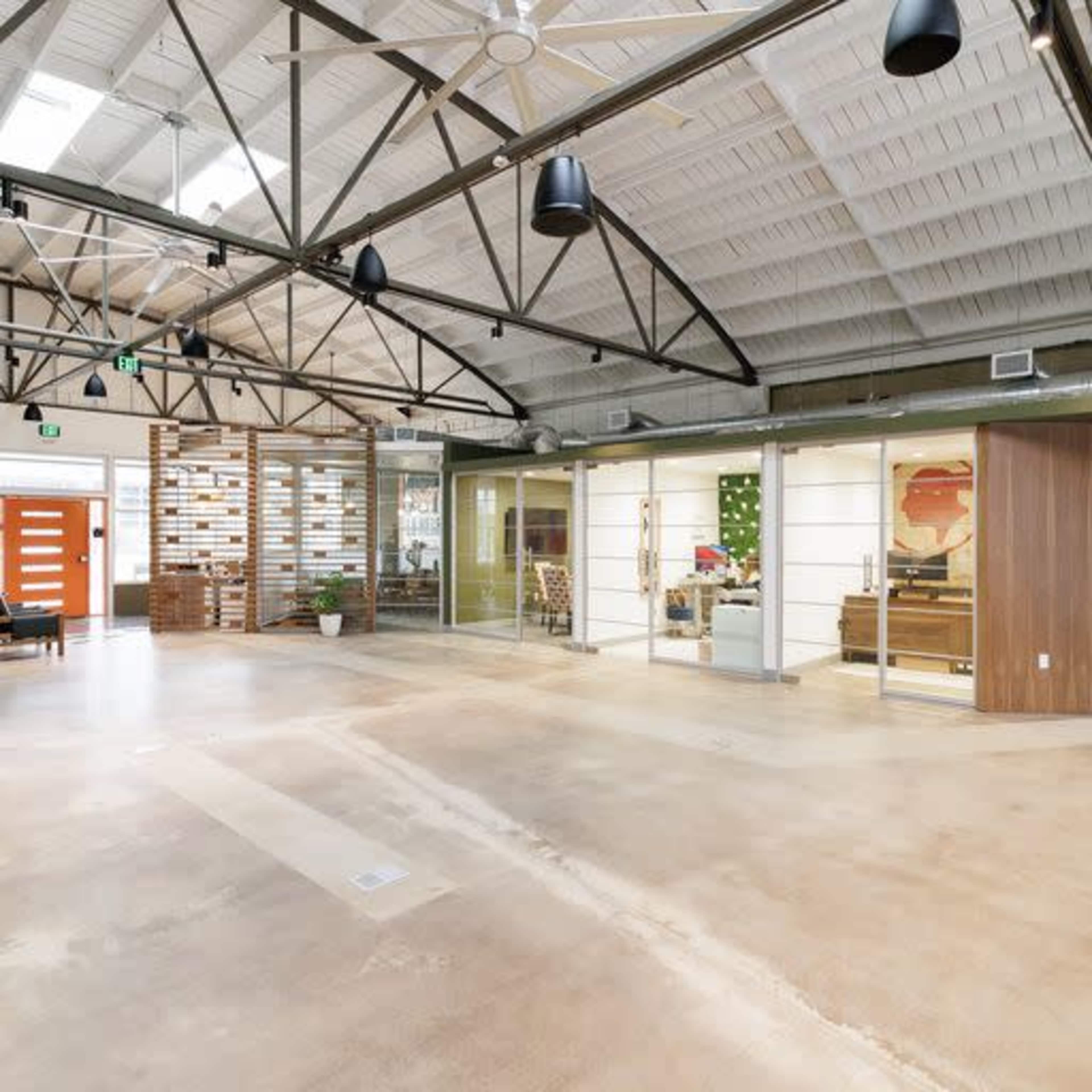 The image shows a spacious, modern office interior with high ceilings, exposed beams, and a mix of open and partitioned work areas.