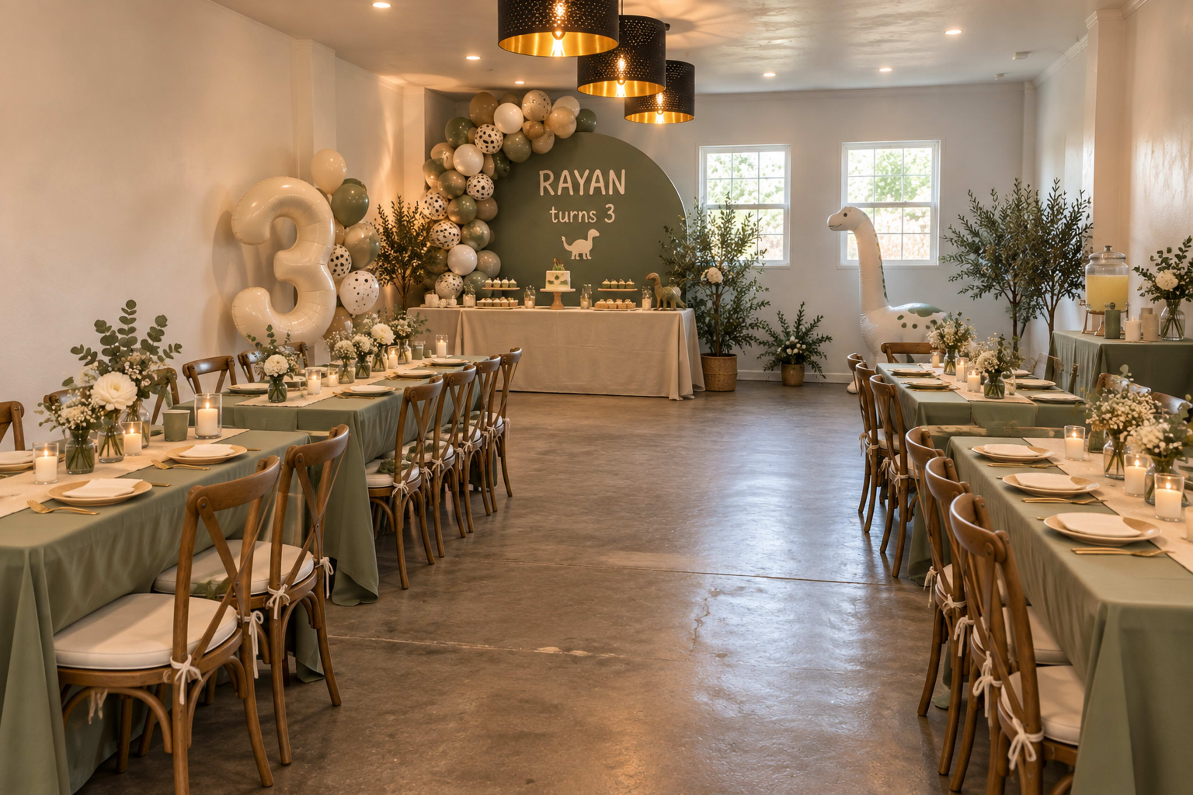 The image shows a decorated event space with two long dining tables, a green and white color scheme, a "Rayan turns 3" backdrop, and a dinosaur-themed decoration.