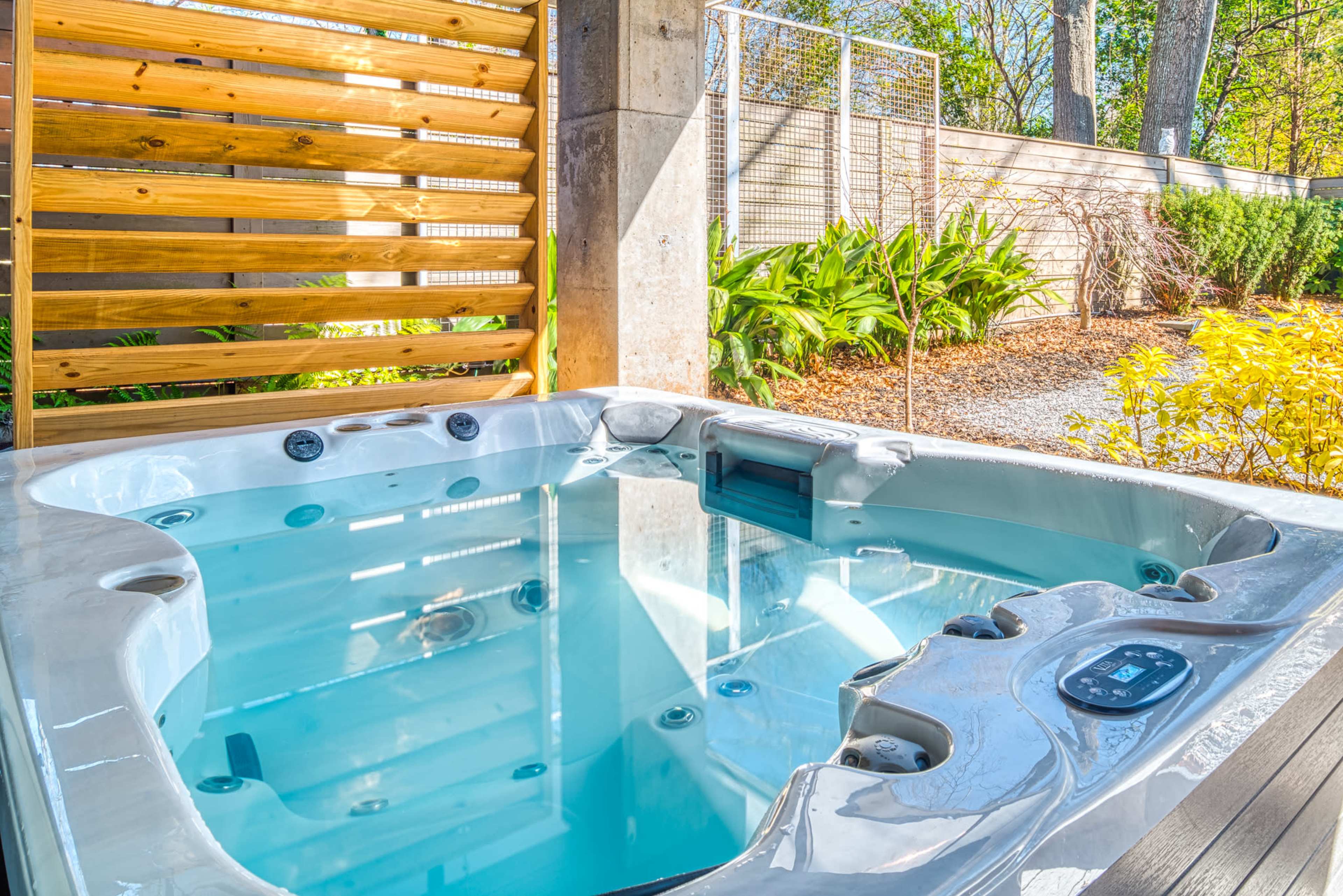 A clear hot tub situated in a well-landscaped outdoor area with wood accents and lush greenery.
