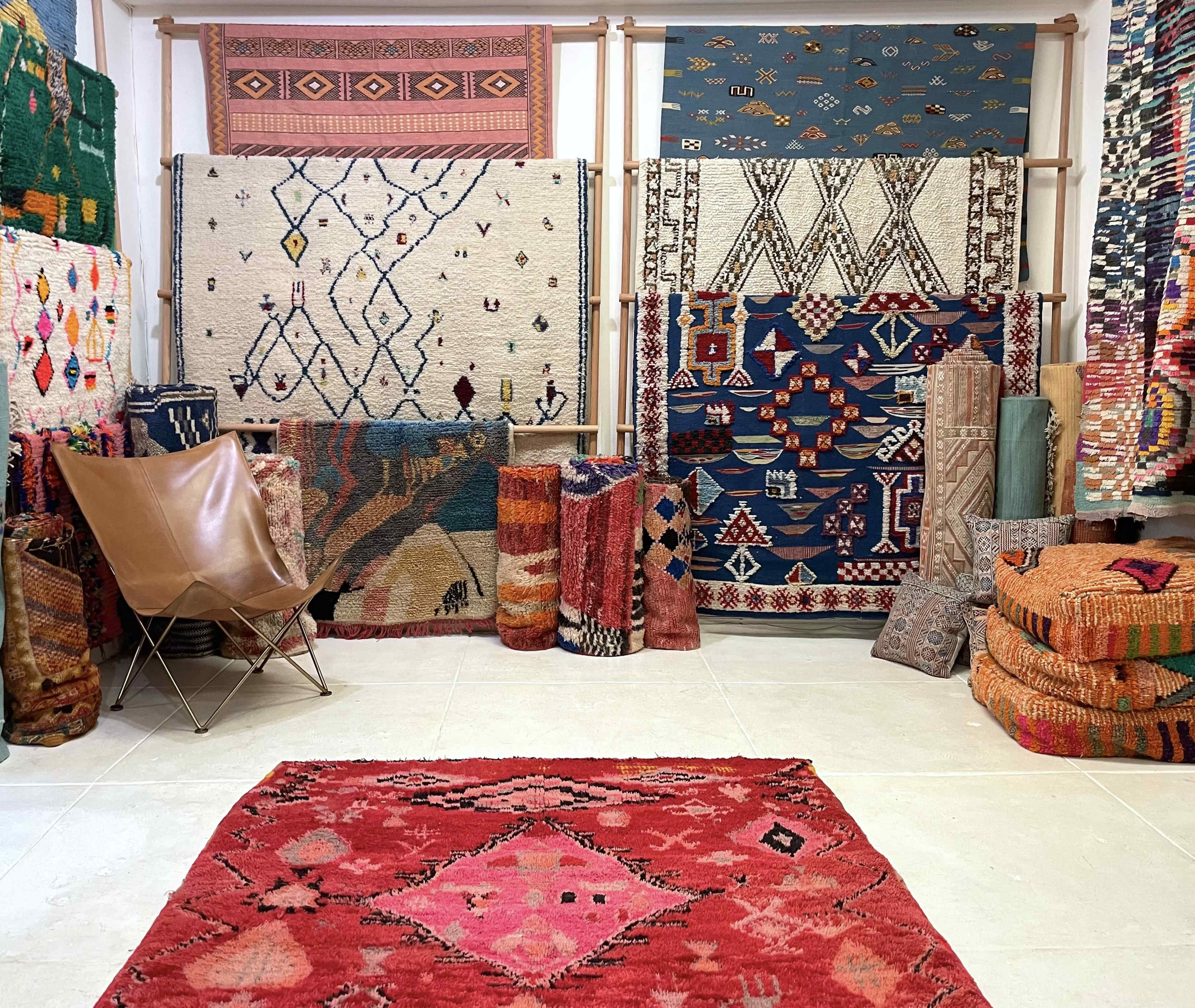 The scene features a room adorned with various colorful rugs and textiles displayed on walls and stacked on the floor.