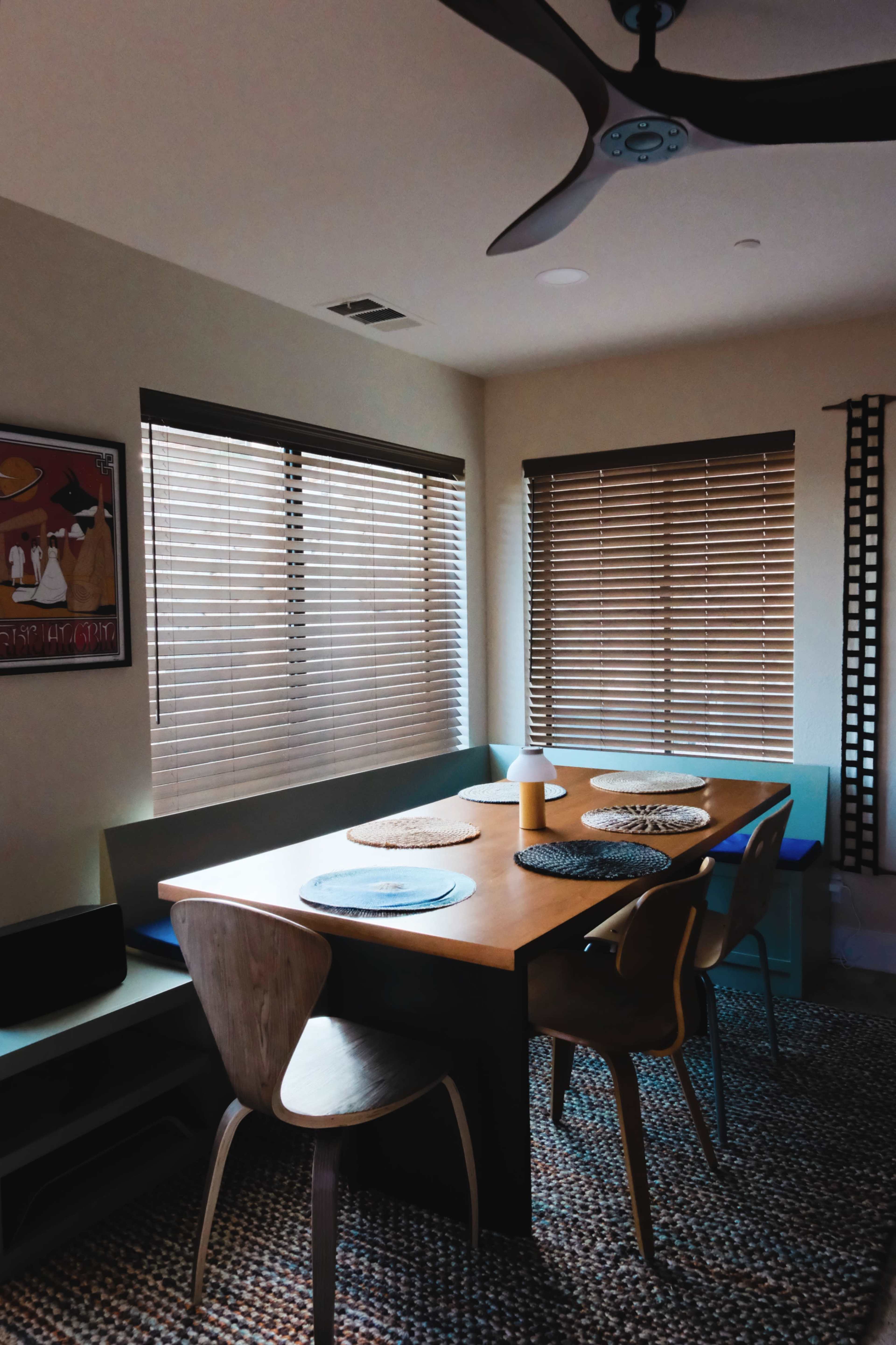 A modern dining area with a wooden table, four chairs, and window blinds.