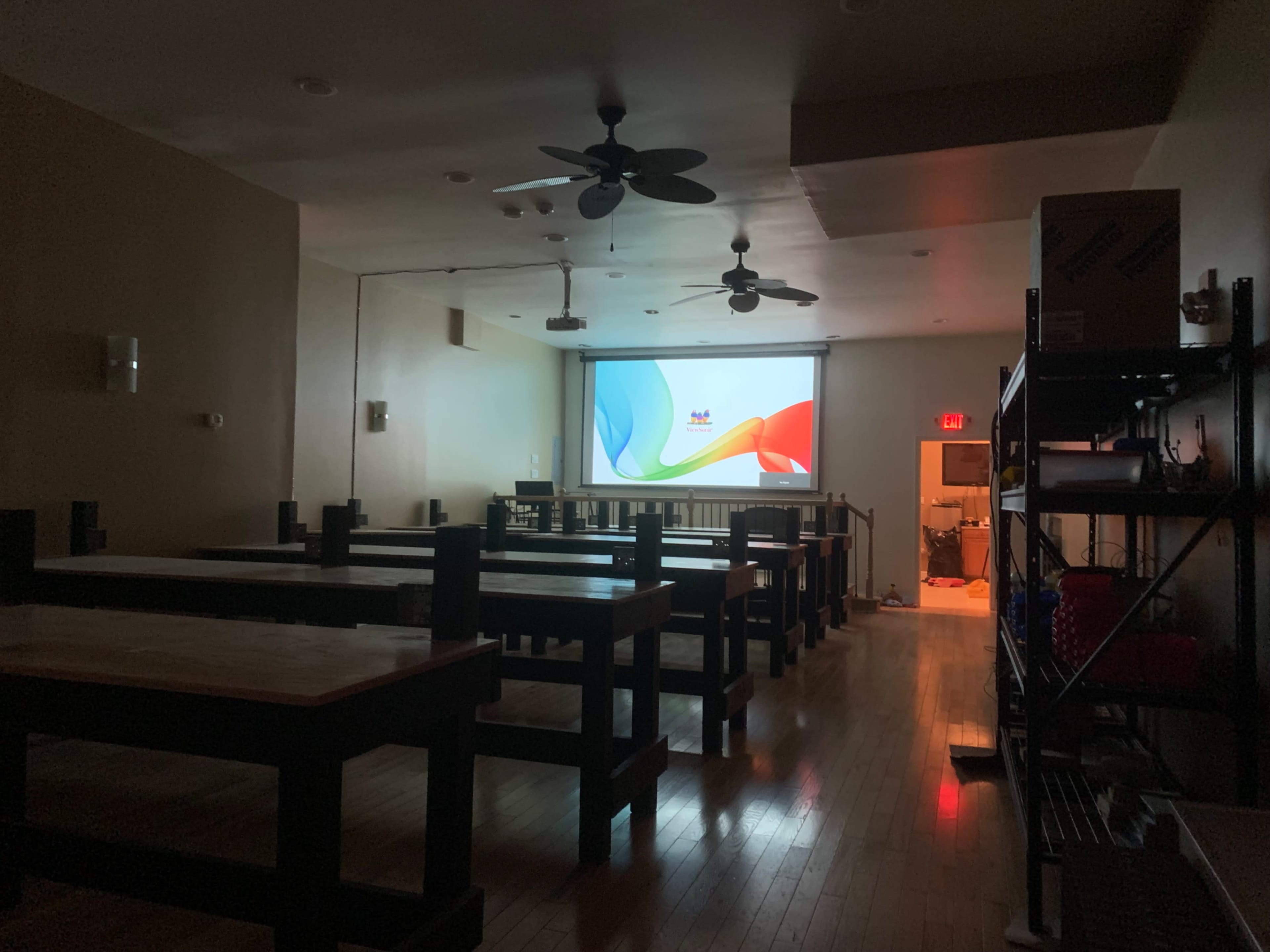 A dimly lit room with rows of wooden tables facing a projector screen displaying a colorful graphic.
