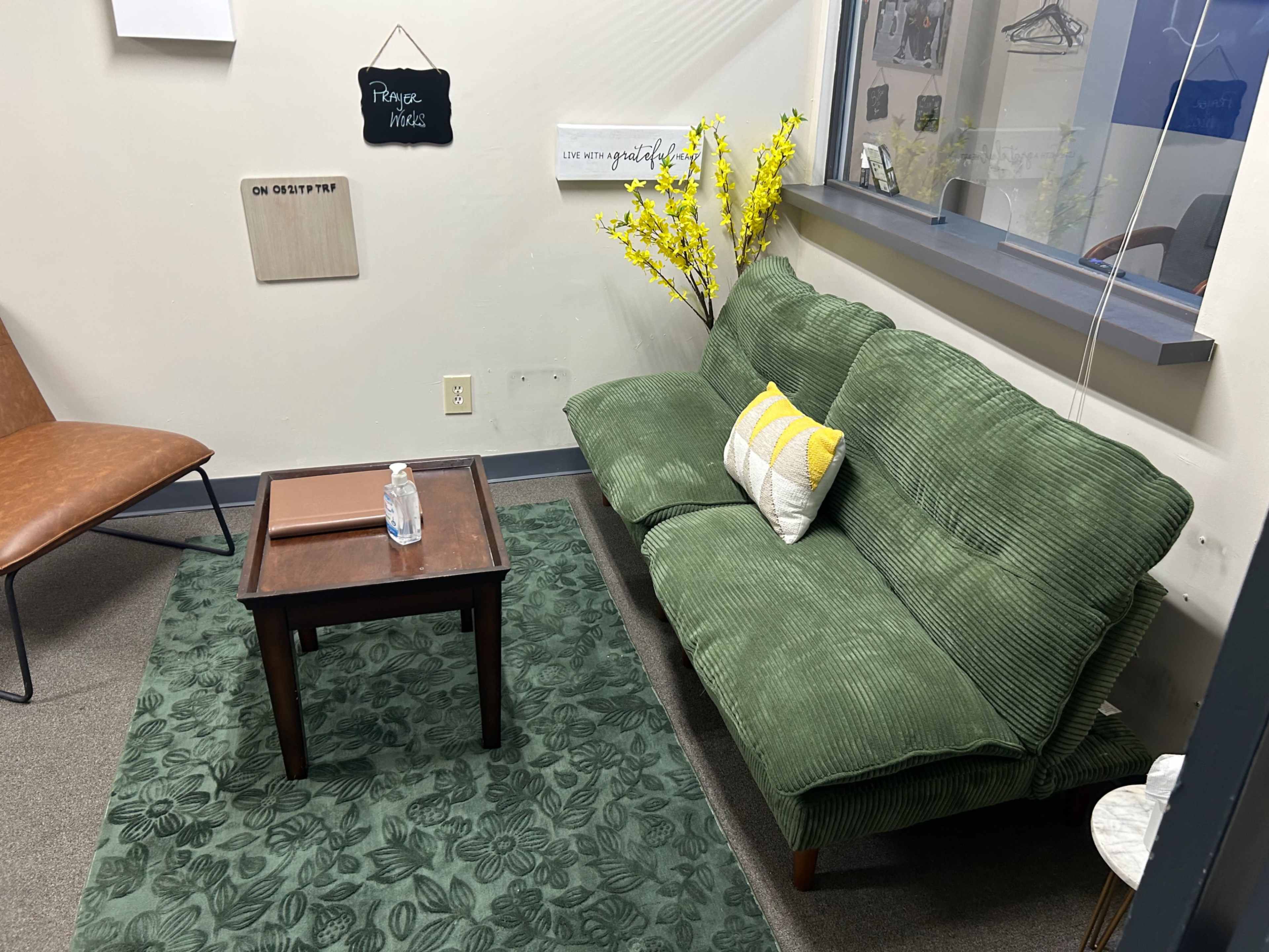 The image shows a small seating area with a green couch, a brown wooden table, and a decorative plant in a corner.